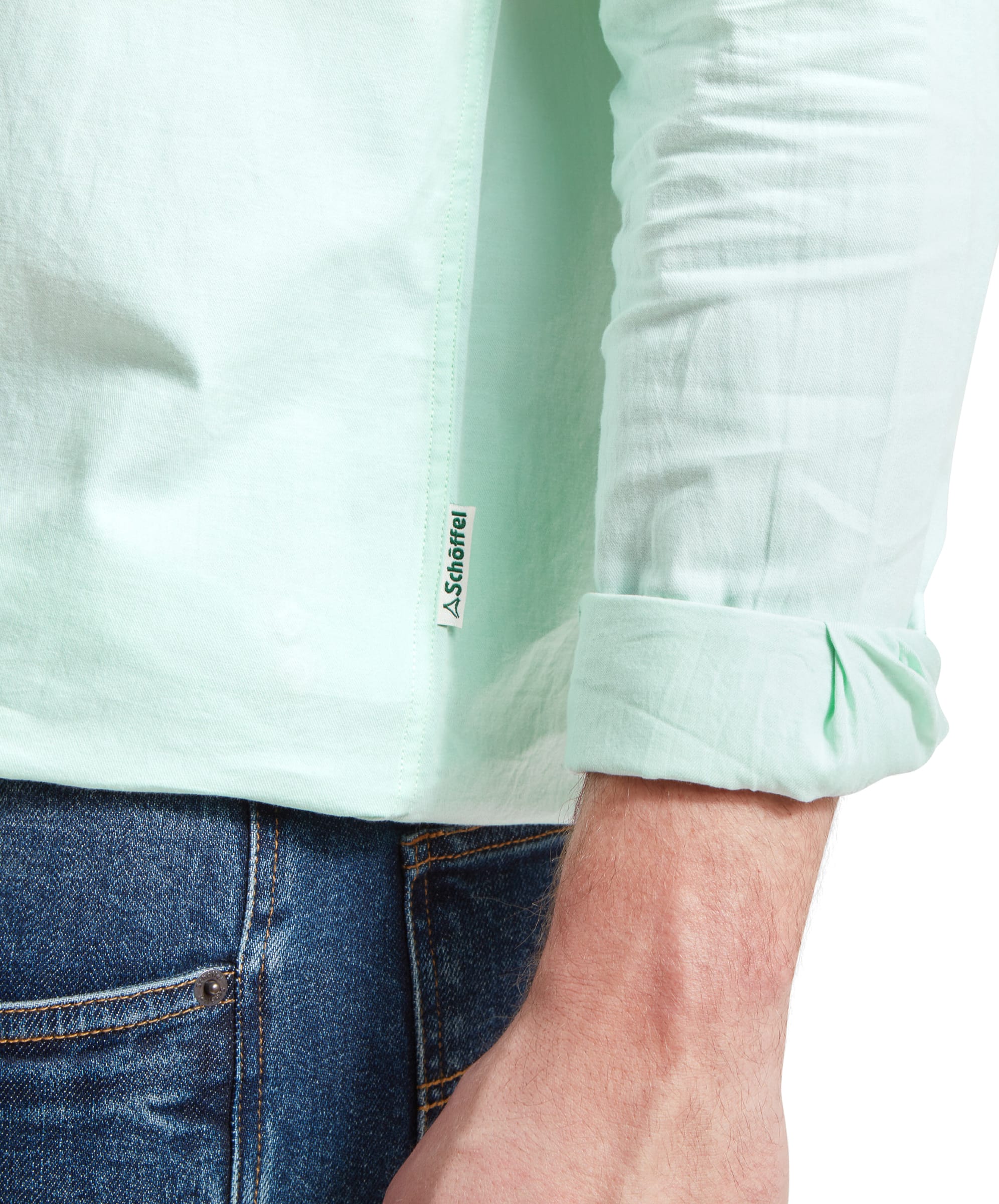 Detailed shot of the hem of the Schöffel Titchwell Tailored Shirt for Men in Greenshirt and the man's arm, showing the sleeve rolled up and a small brand label near the shirt's side seam. The shirt is paired with blue jeans.