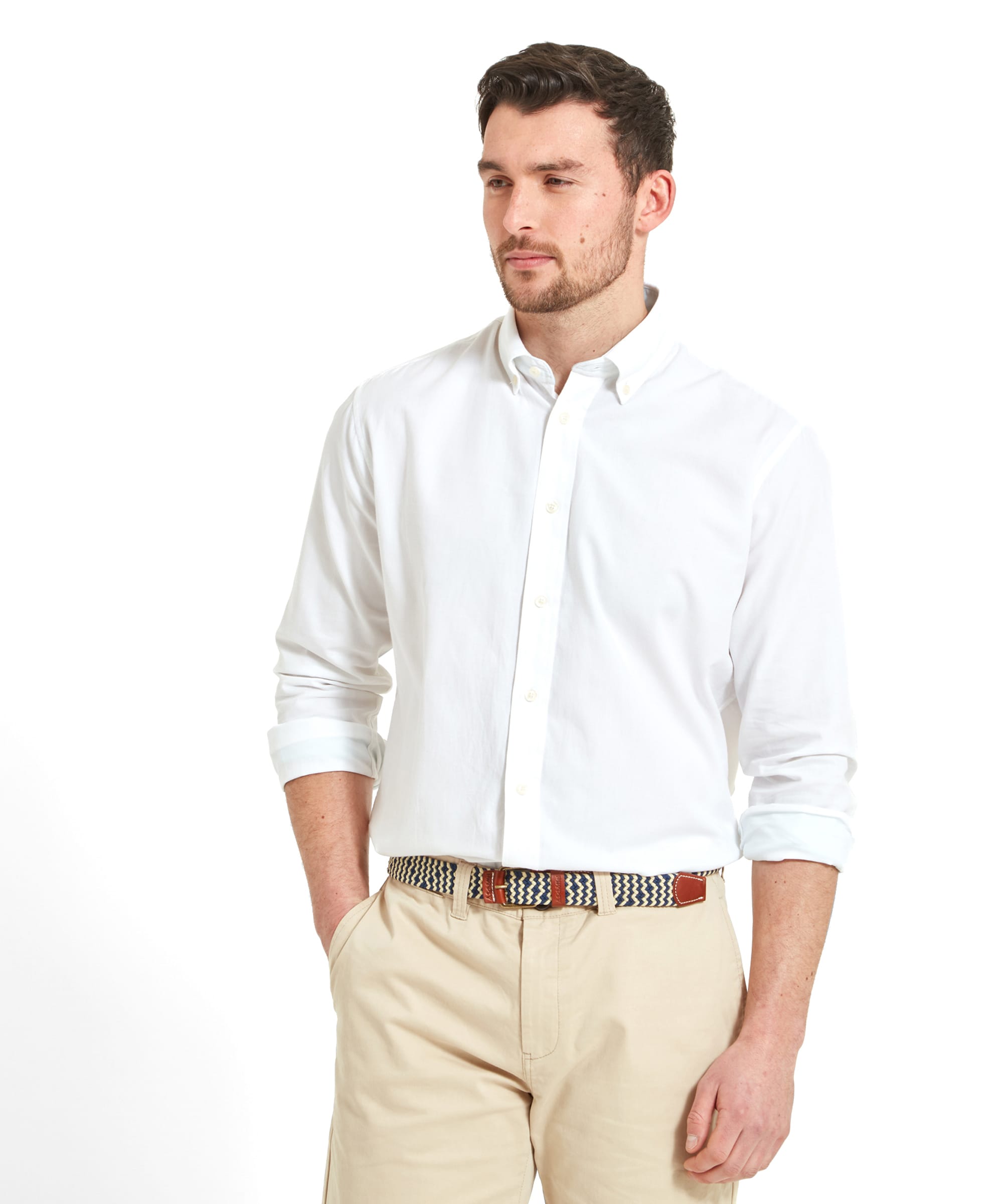 The man is wearing a neatly pressed, Schöffel Titchwell Tailored Shirt for Men in White with a collar. The shirt is complemented by a pair of beige shorts. He has a calm expression and is standing with one hand in his pocket. His overall appearance is clean and casual yet elegant.