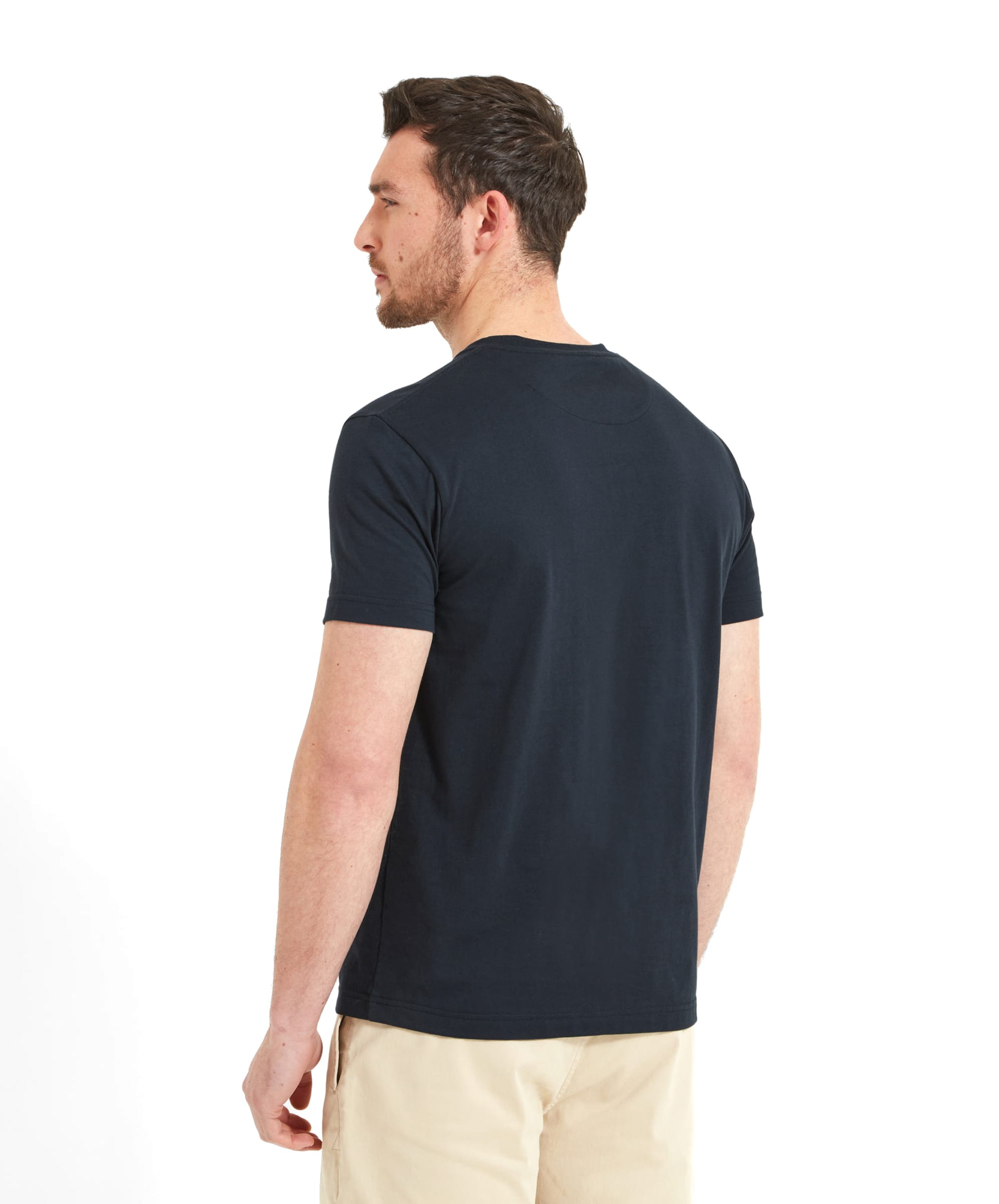 A back view of the man in the Schöffel Towan T-Shirt for Men in Navy and beige shorts. He stands casually, showing the simple design of the T-shirt and the back pockets of the shorts.