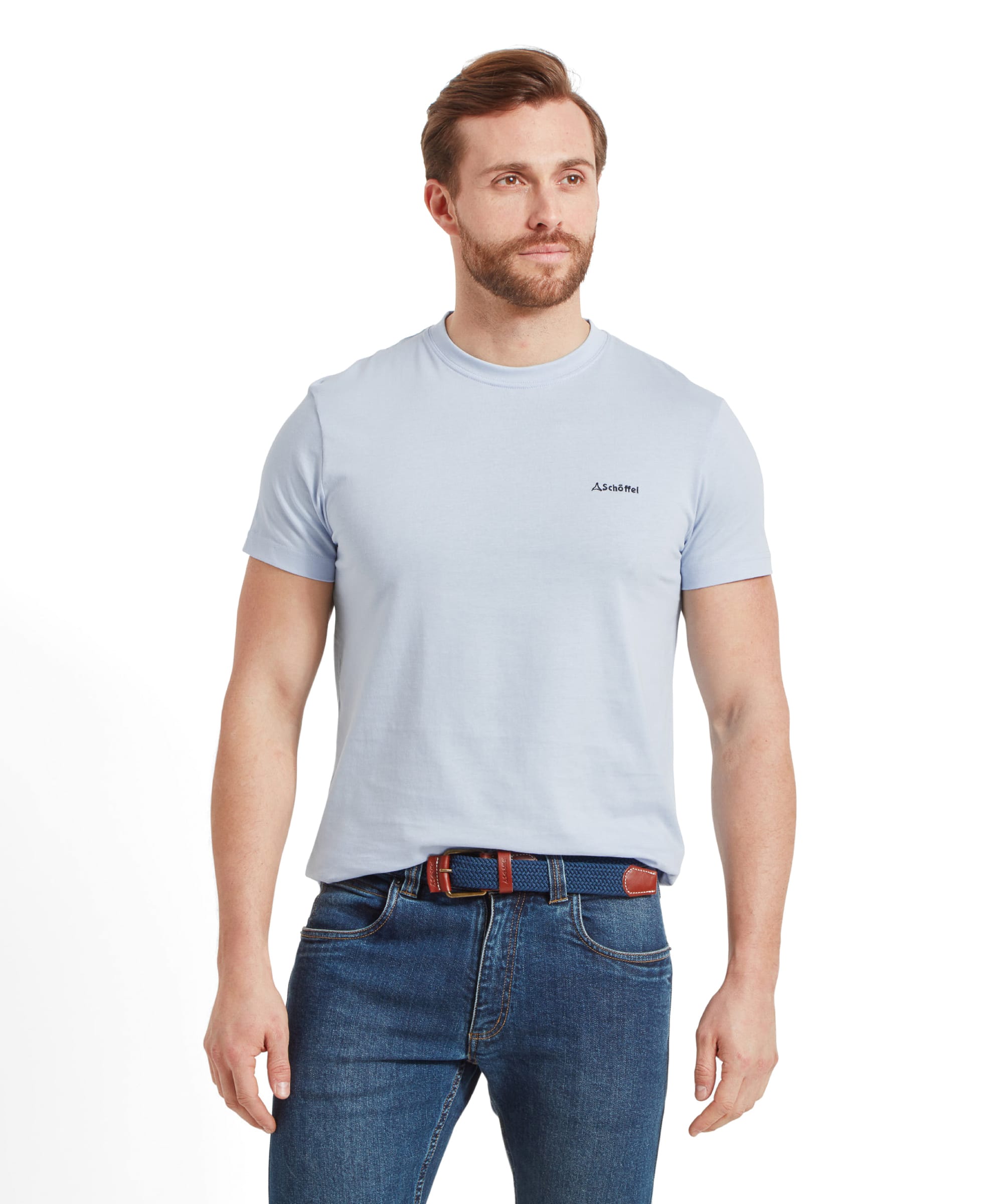 A man is standing wearing a Schöffel Trevone T-Shirt for Men in Blue with a small logo on the chest and blue jeans. He has a neutral expression and his hands in his pockets.