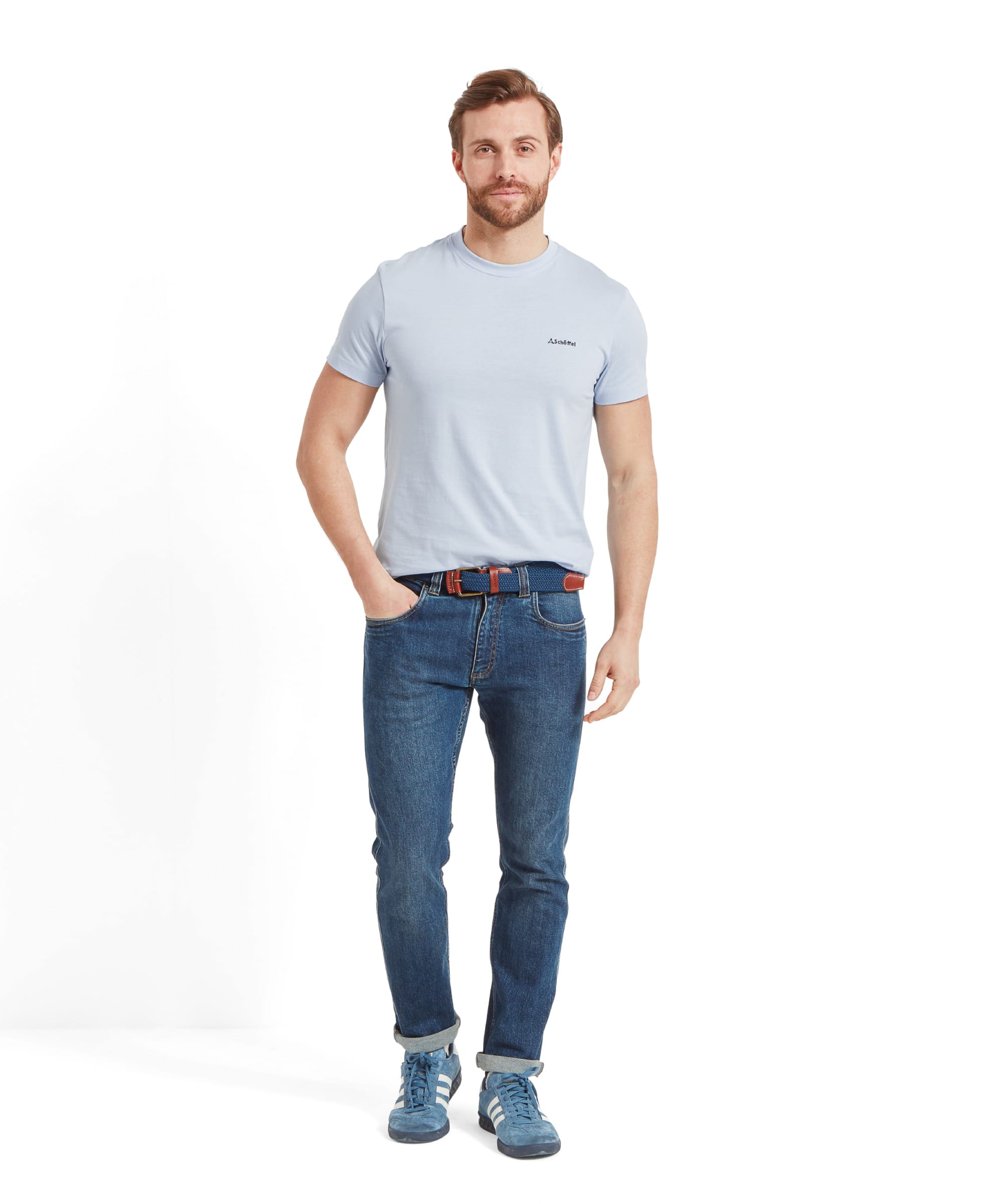 The full body view of the man, showcasing the Schöffel Trevone T-Shirt for Men in Blue paired with jeans and blue trainers, standing casually with one hand in his pocket.