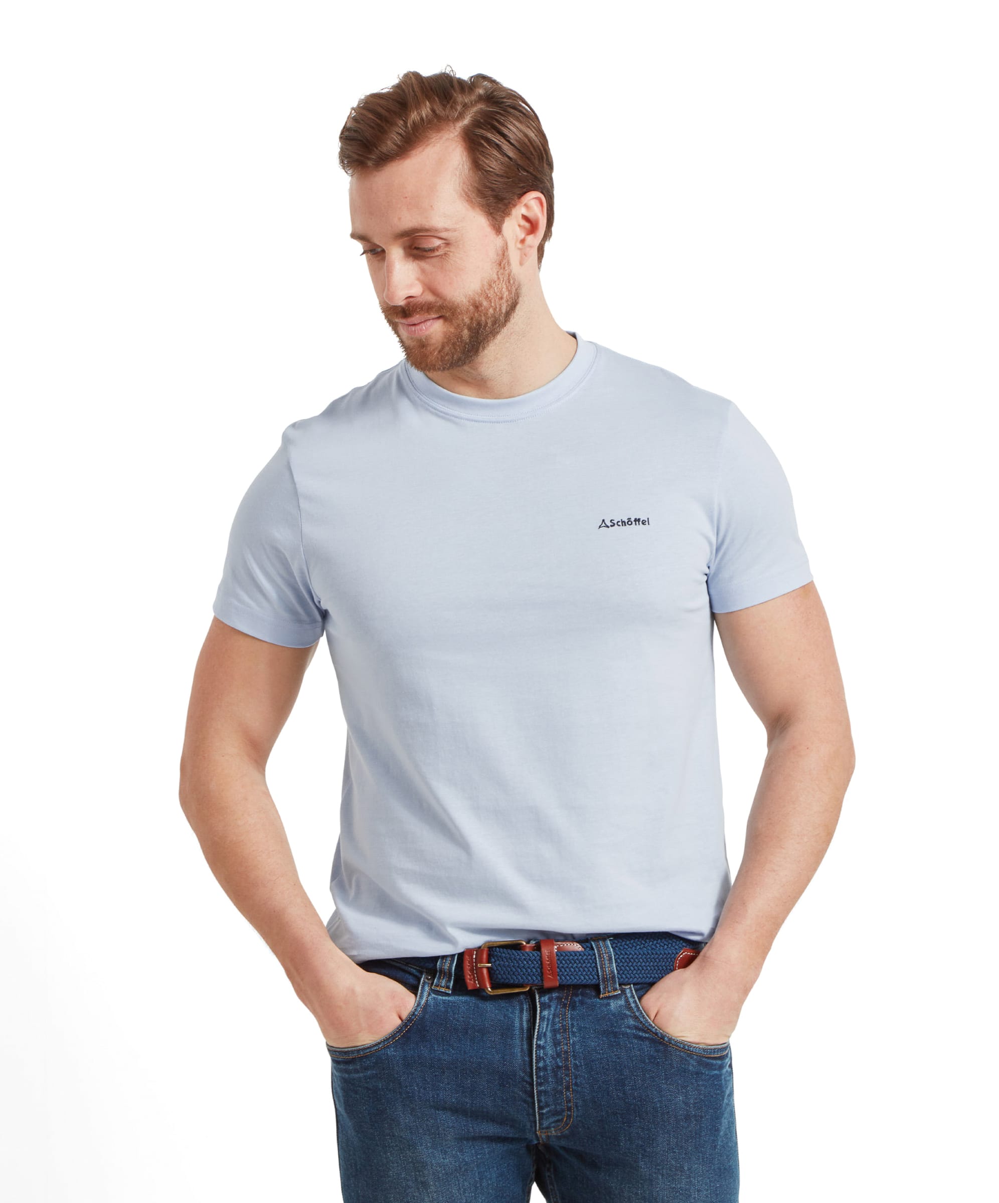 A smiling man looks down to his left in a Schöffel Trevone T-Shirt for Men in Blue and jeans, standing with both hands in his pockets.