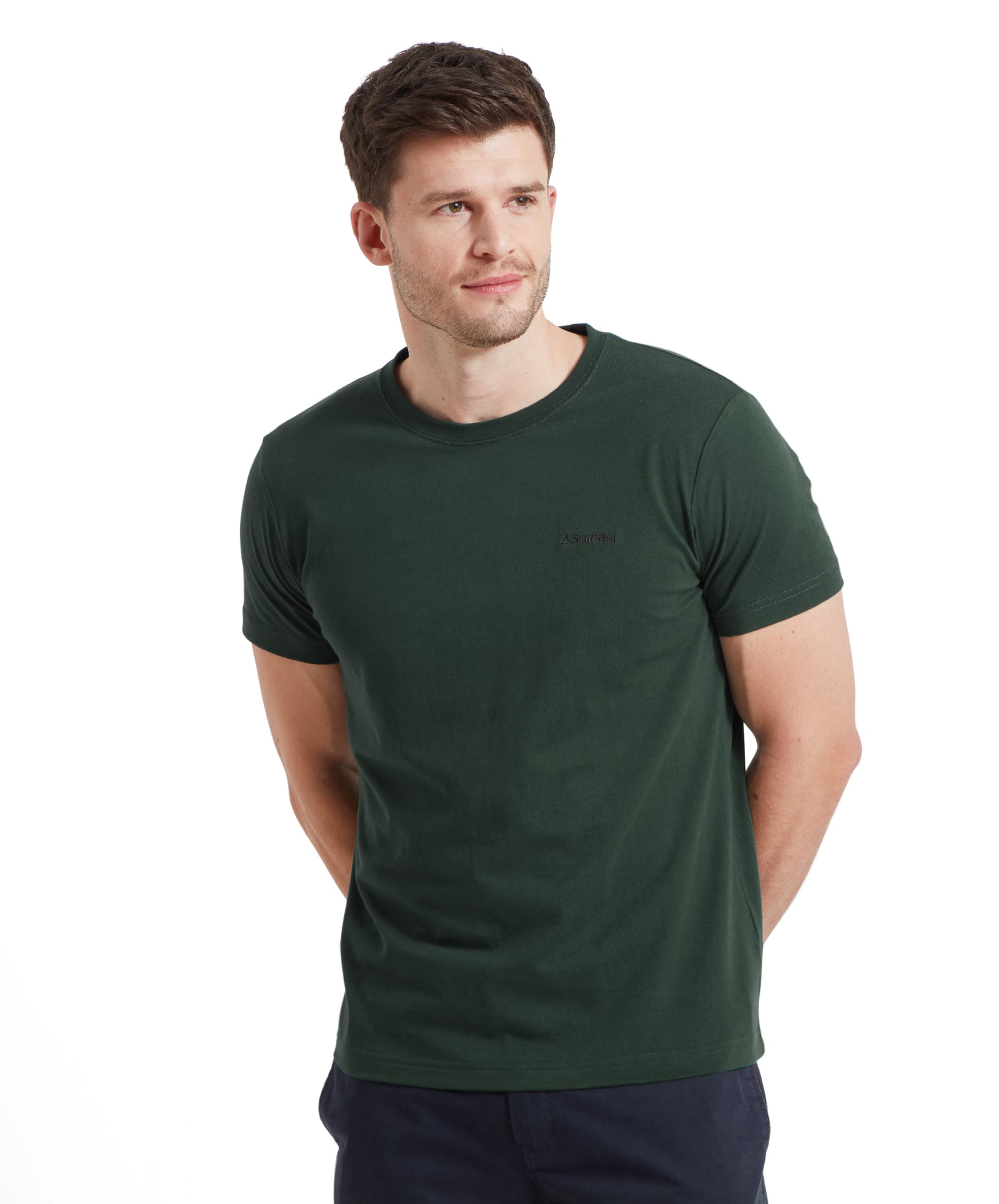 A man wearing a Schöffel Trevone T-Shirt for Men in Green stands with his hands behind his back. The t-shirt features a small embroidered logo on the chest. He has short hair and is looking slightly to the right.