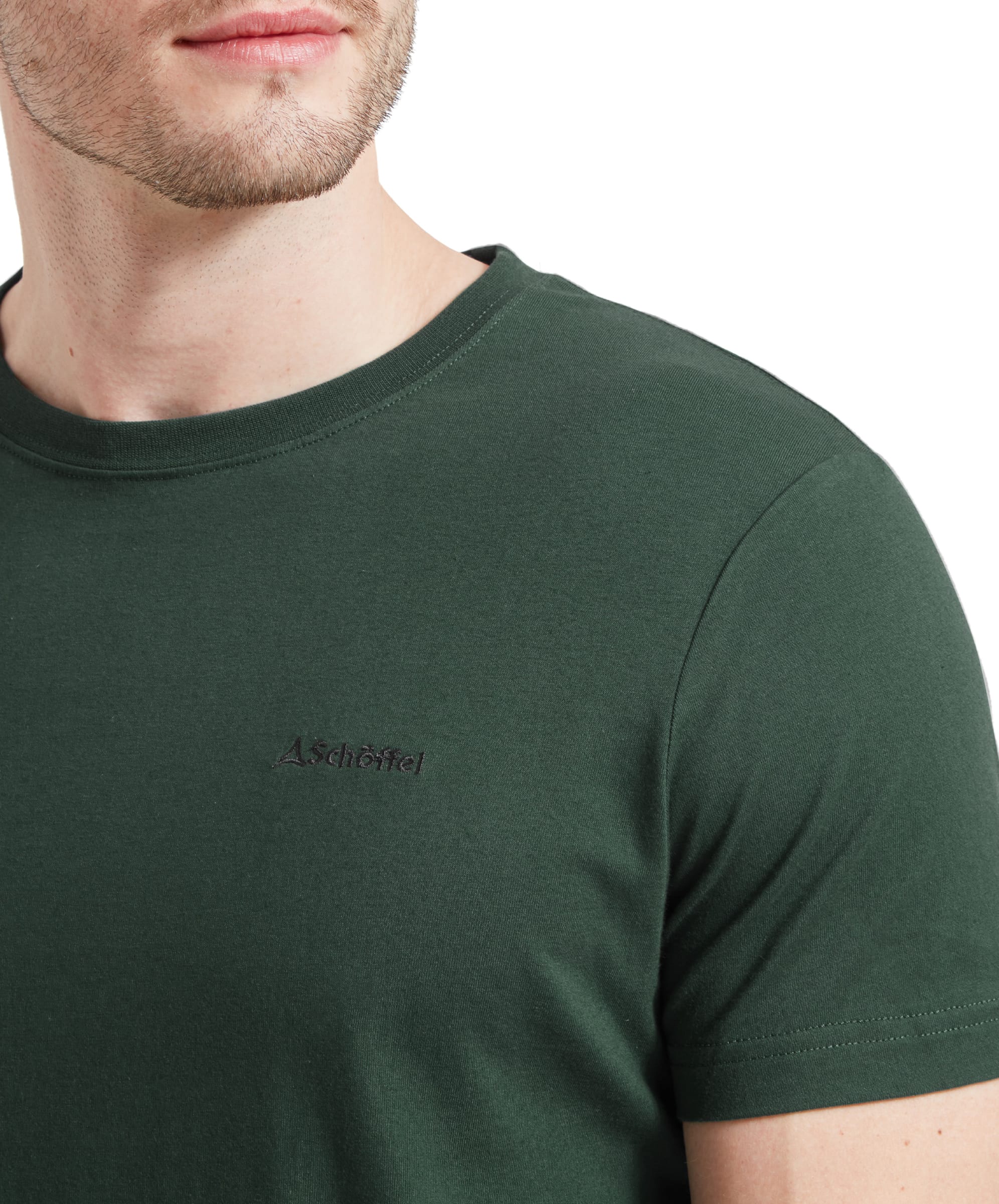 Close-up of a man’s chest, highlighting the small, embroidered logo on the left side of his Schöffel Trevone T-Shirt for Men in Green. The focus is on the shirt’s detail and texture.