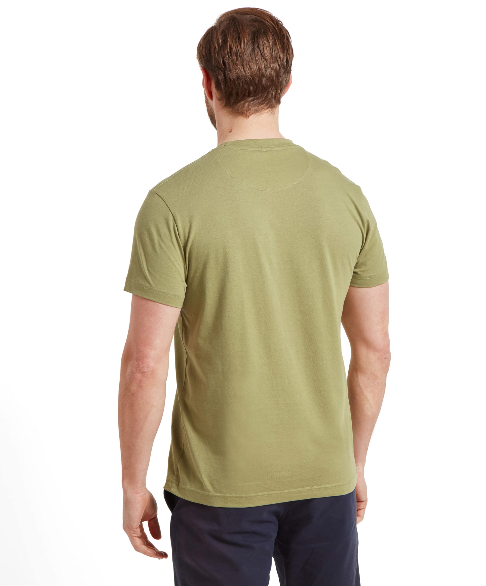 The back view of the man, highlighting the plain back of the Schöffel Trevone T-Shirt for Men in Olive Green and the fit of the navy shorts. The T-shirt fits snugly around the shoulders and upper back.