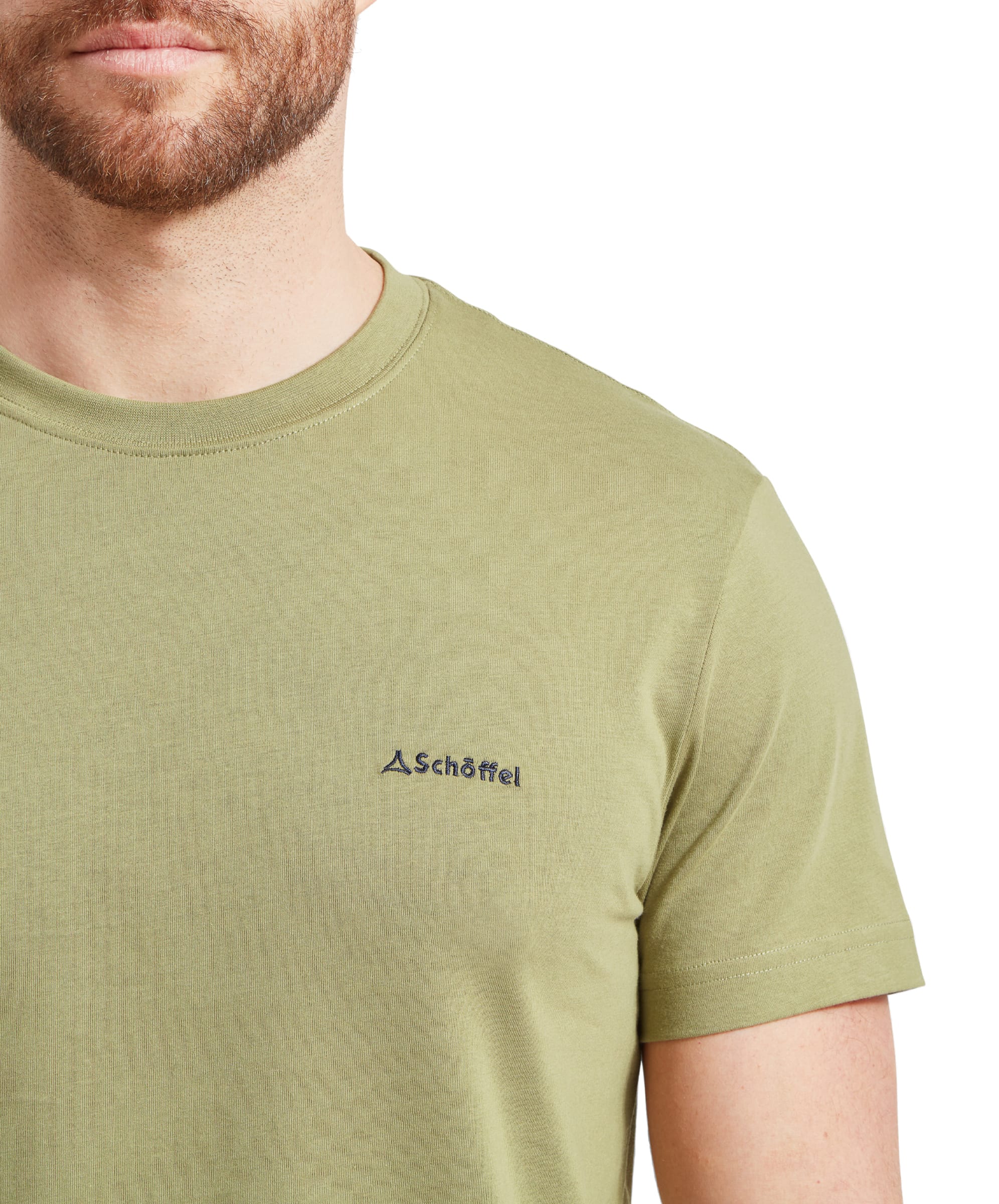 A close-up of the man's chest area, focusing on the Schöffel logo embroidered in a contrasting color on the left side of the Schöffel Trevone T-Shirt for Men in Olive Green. The logo is subtle and blends well with the T-shirt's color.