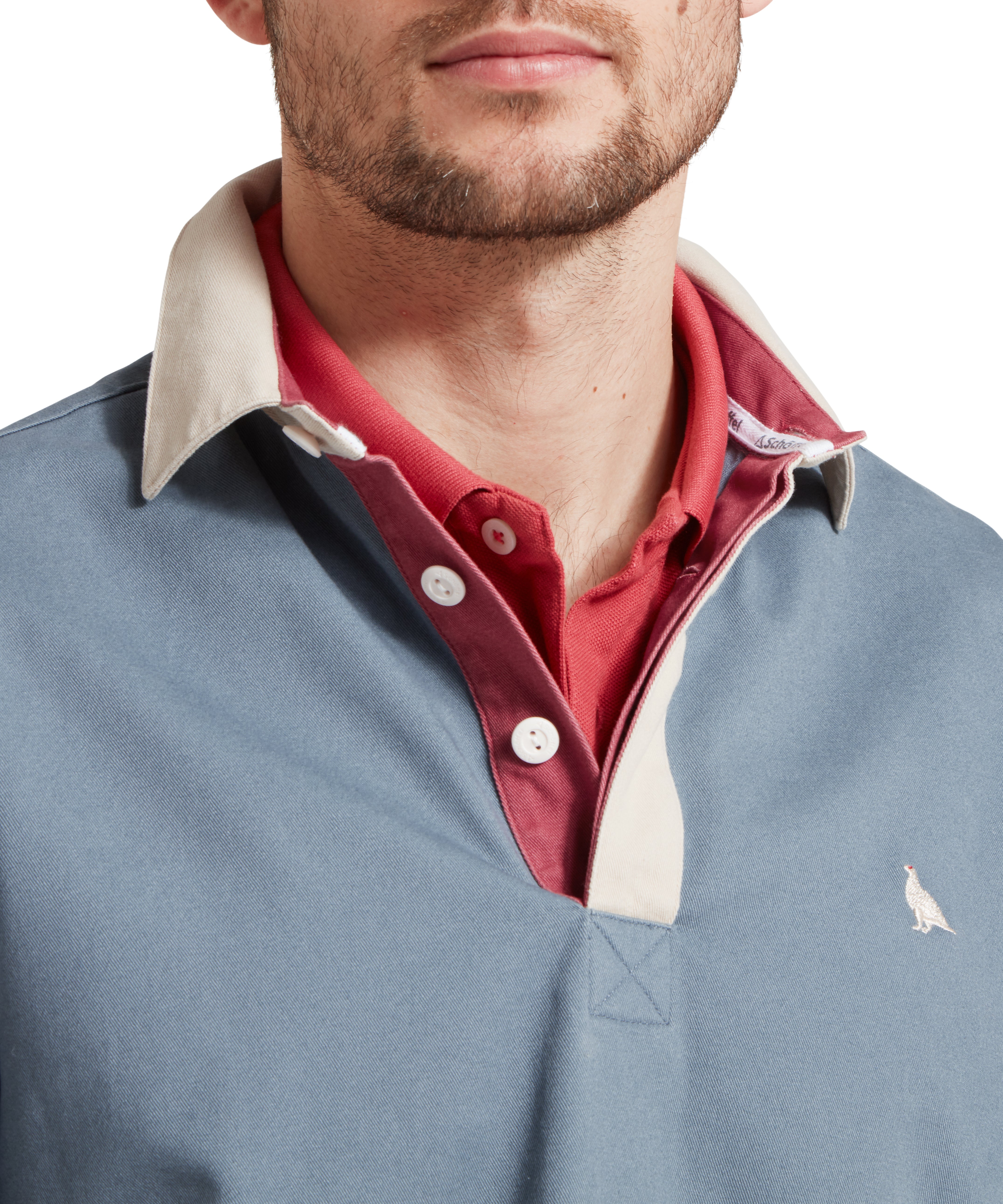 Close up image of a male model wearing a blue Schöffel sweatshirt with red and white stripe detailing on the sleeves and small embroidered bird logo on the chest. It is paired with a red polo. Image highlights the button up collar.