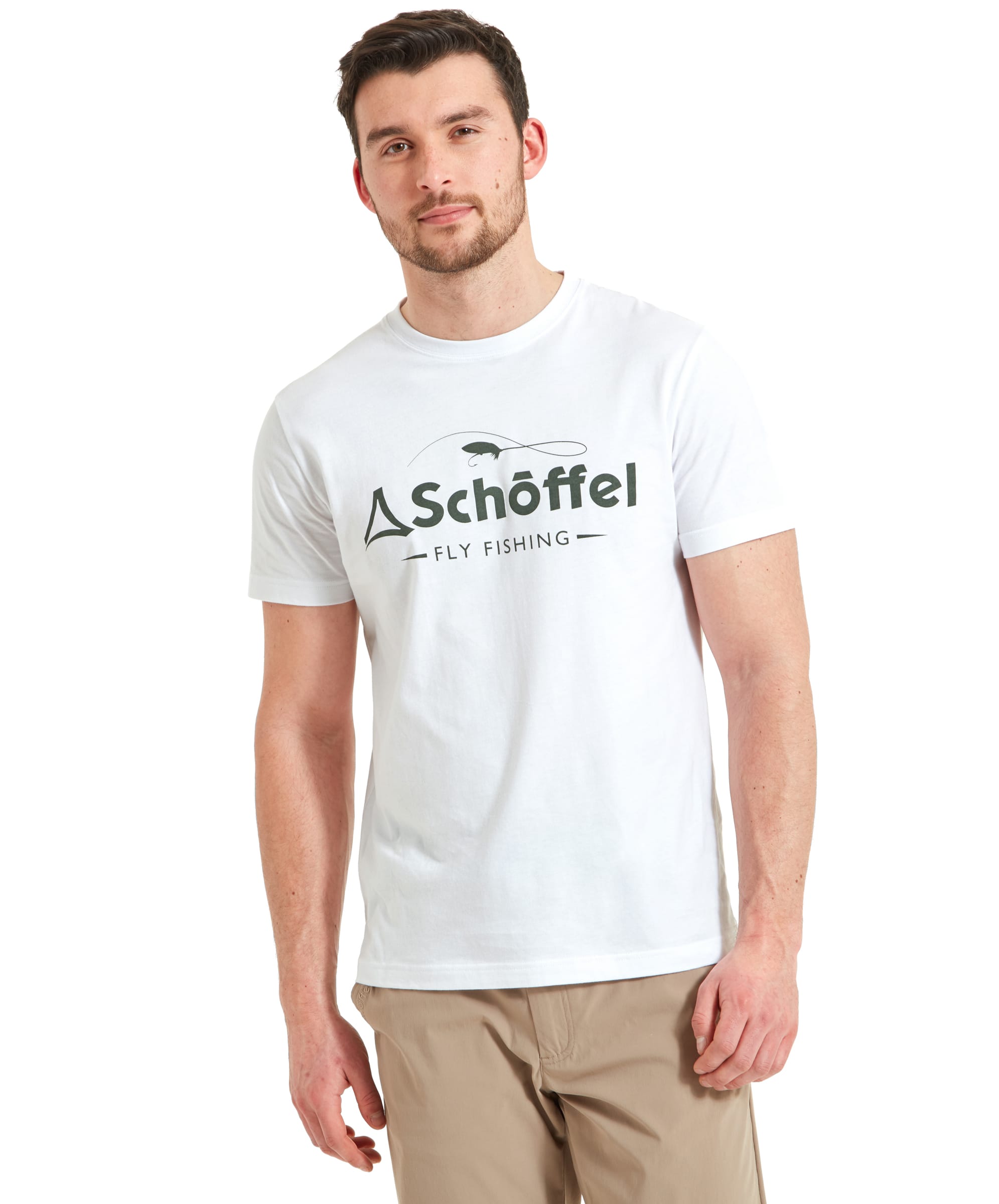 A man is wearing a Schöffel Tyne T-Shirt for Men in White with "Schöffel Fly Fishing" printed on the front in green. He stands casually with a slight smile and a relaxed pose. The t-shirt is paired with beige trousers, and his hair is neatly styled. The image is bright and the subject is well-lit against a plain background.