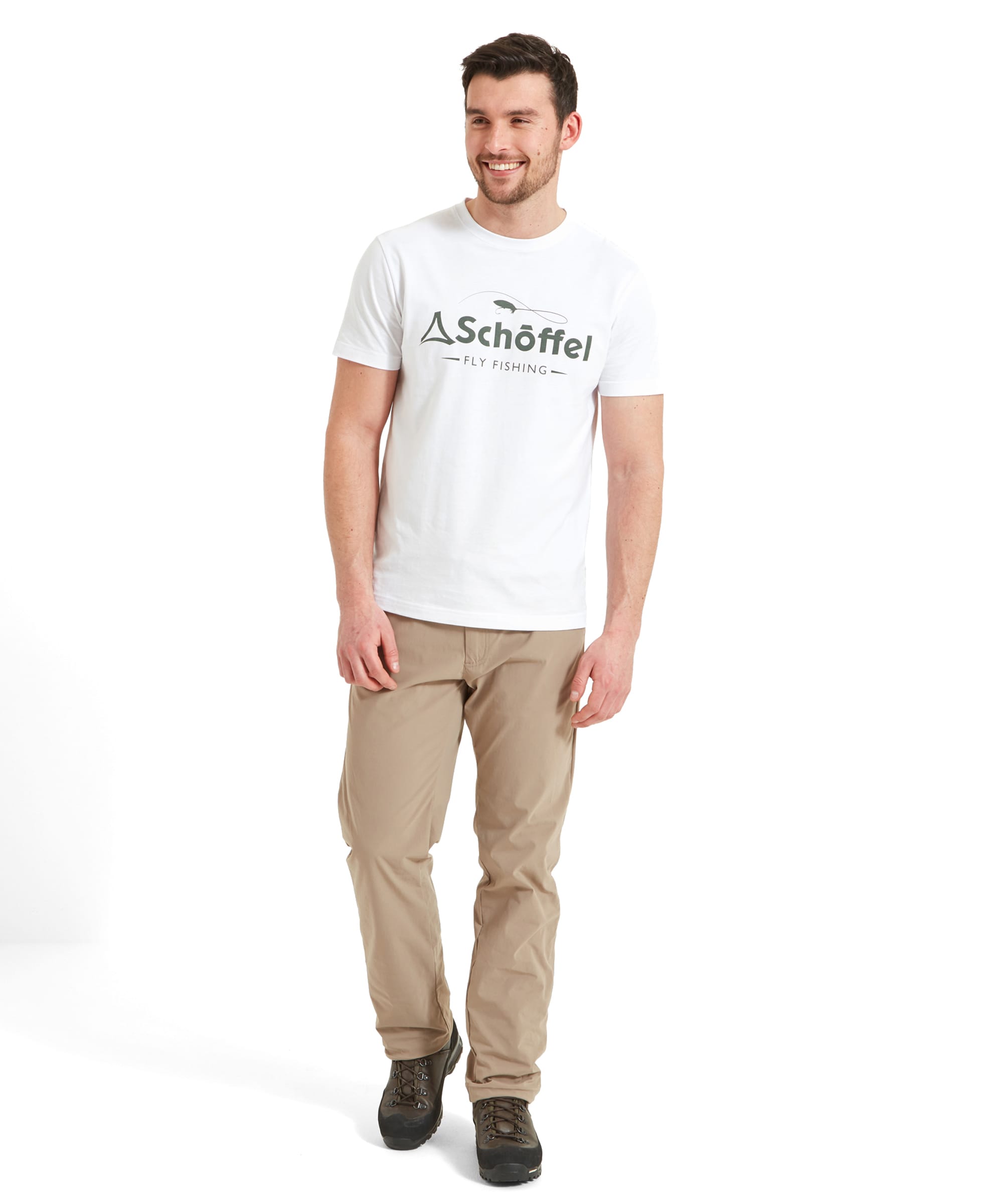 The same man is shown standing in a full-body shot. He is smiling and looking to the side. The Schöffel Tyne T-Shirt for Men in White with the "Schöffel Fly Fishing" logo is paired with beige trousers and brown hiking shoes. The background is simple, keeping the focus on the outfit.