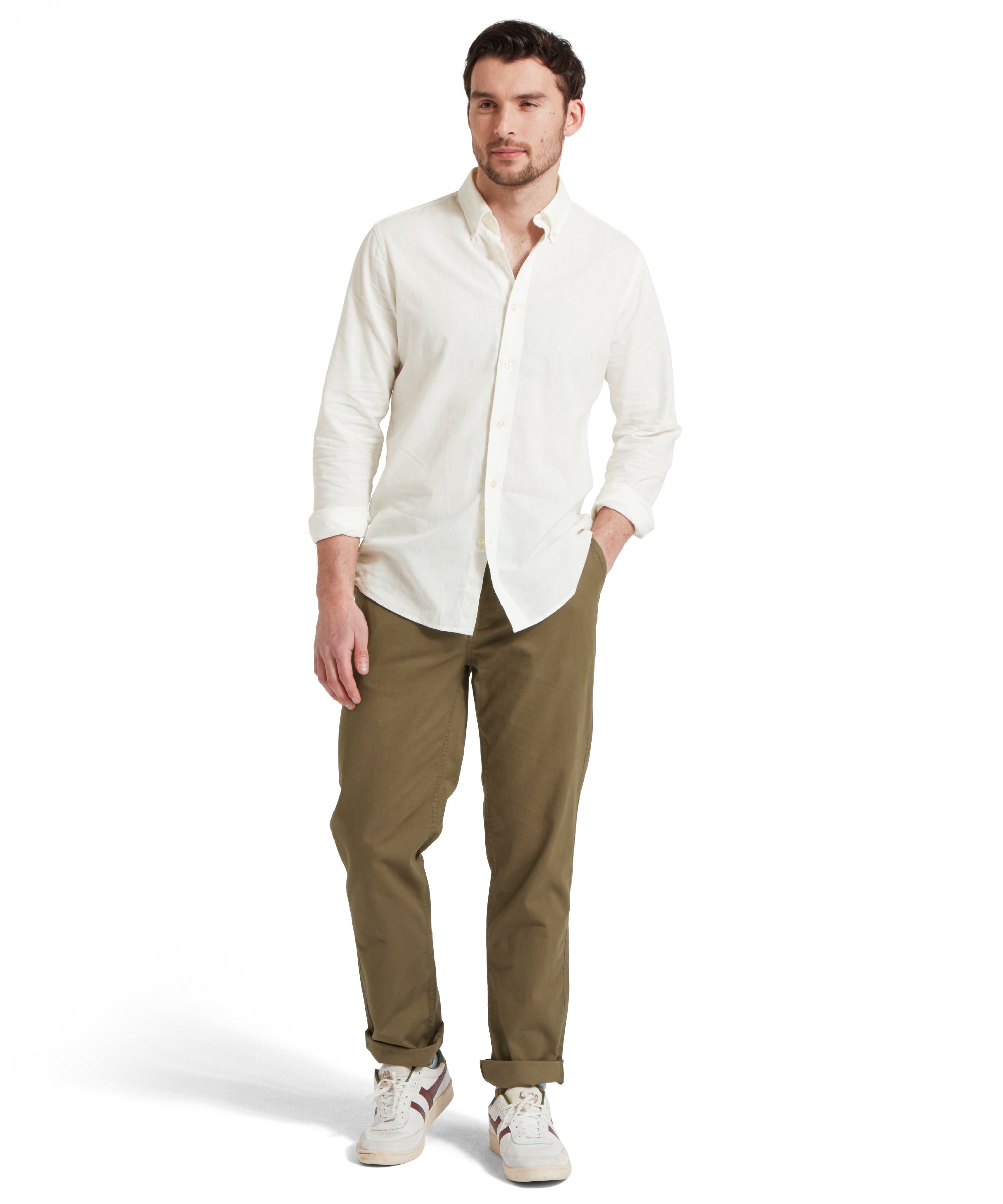 Full-height of a male model wearing a white Schöffel shirt paired with dark green chinos trousers and white trainers. He is standing in a relaxed pose with one hand in his pocket.