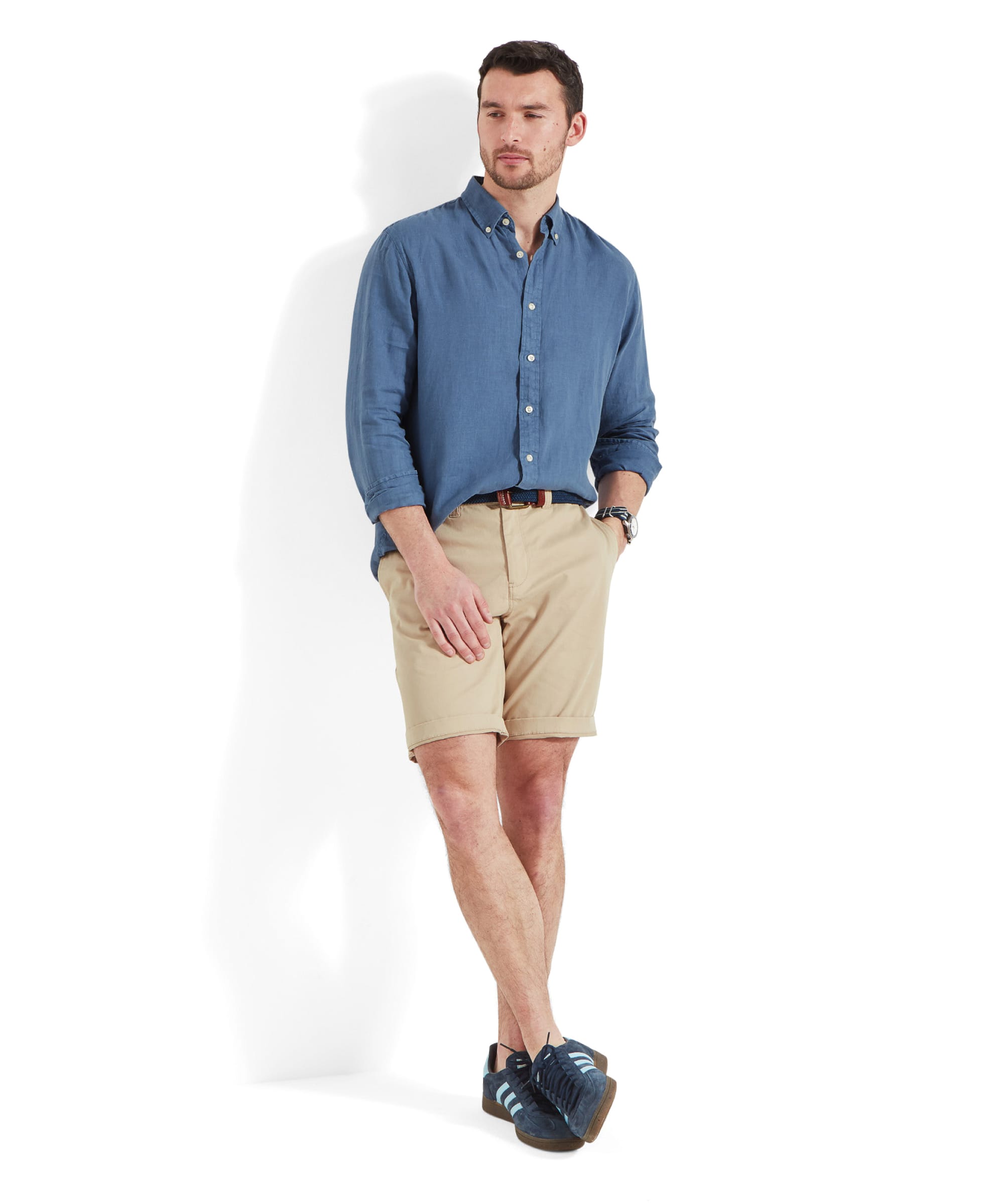 The same man, now wearing the Schöffel Walsingham Linen Shirt for Men in Blue untucked, paired with beige shorts and blue casual shoes. He has his hands in his pockets, exuding a relaxed vibe.