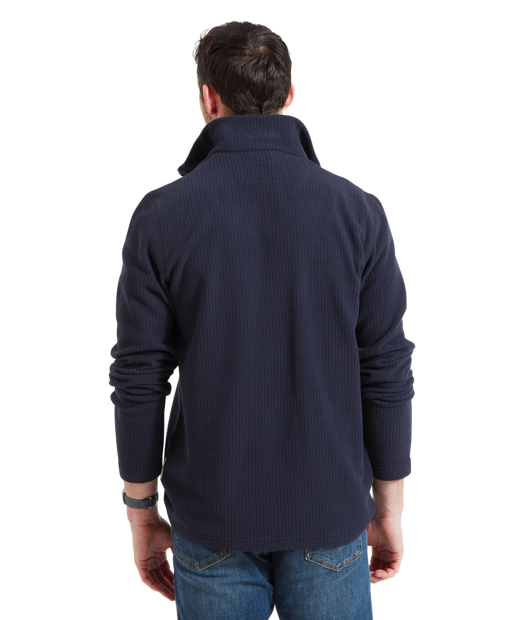 The back view of the male model shows the full length of the Schöffel Welland Lightweight Fleece for Men in Blue, highlighting its relaxed fit and ribbed texture. The model's hands are in his pockets, and he wears blue jeans, completing the casual outfit.