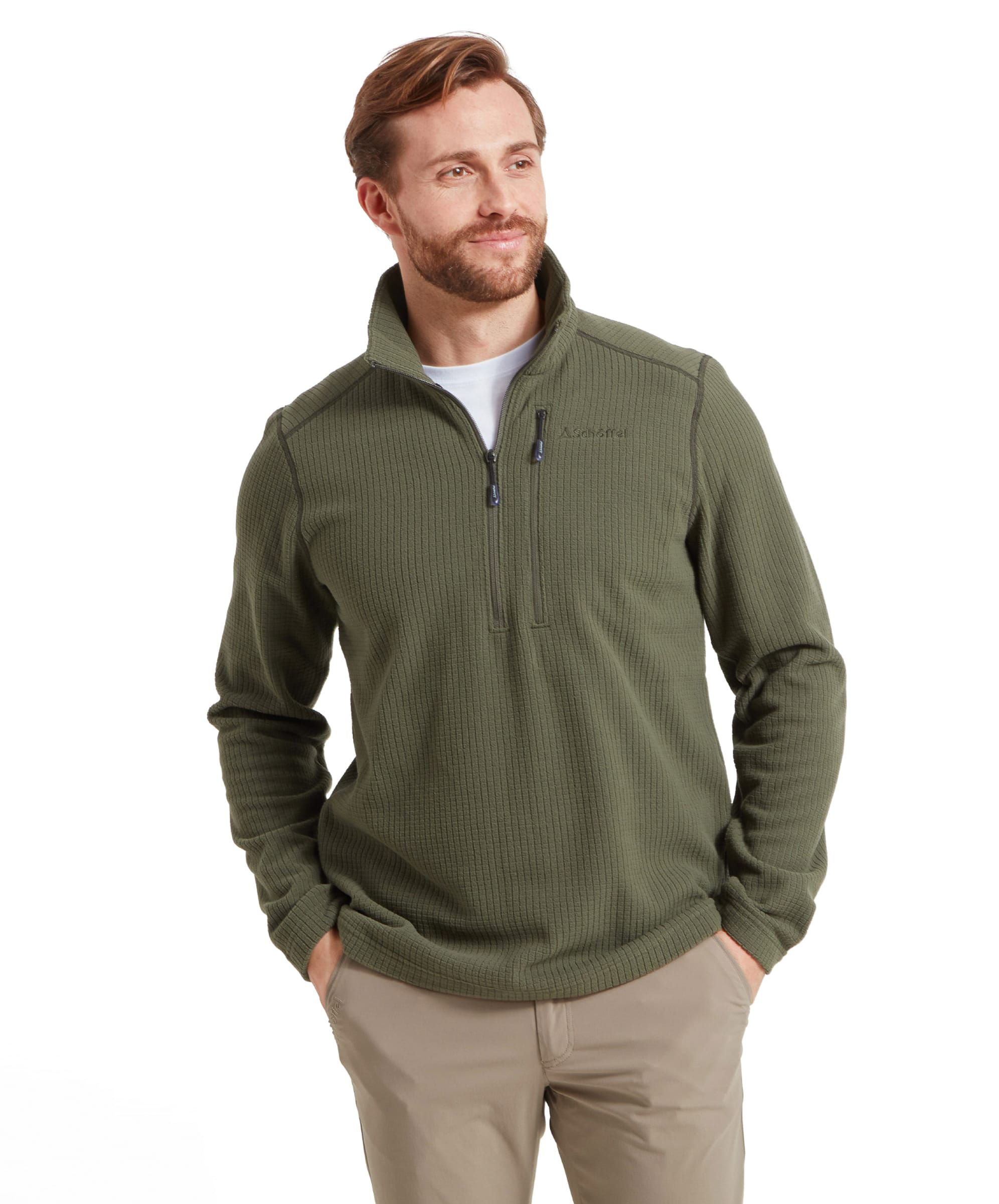 A male model is wearing a Schöffel Welland Lightweight Fleece for Men in Green with a quarter-zip front. The fleece has a textured pattern and a high collar. The model is smiling slightly and has his hands in his pockets, giving a relaxed and casual look.