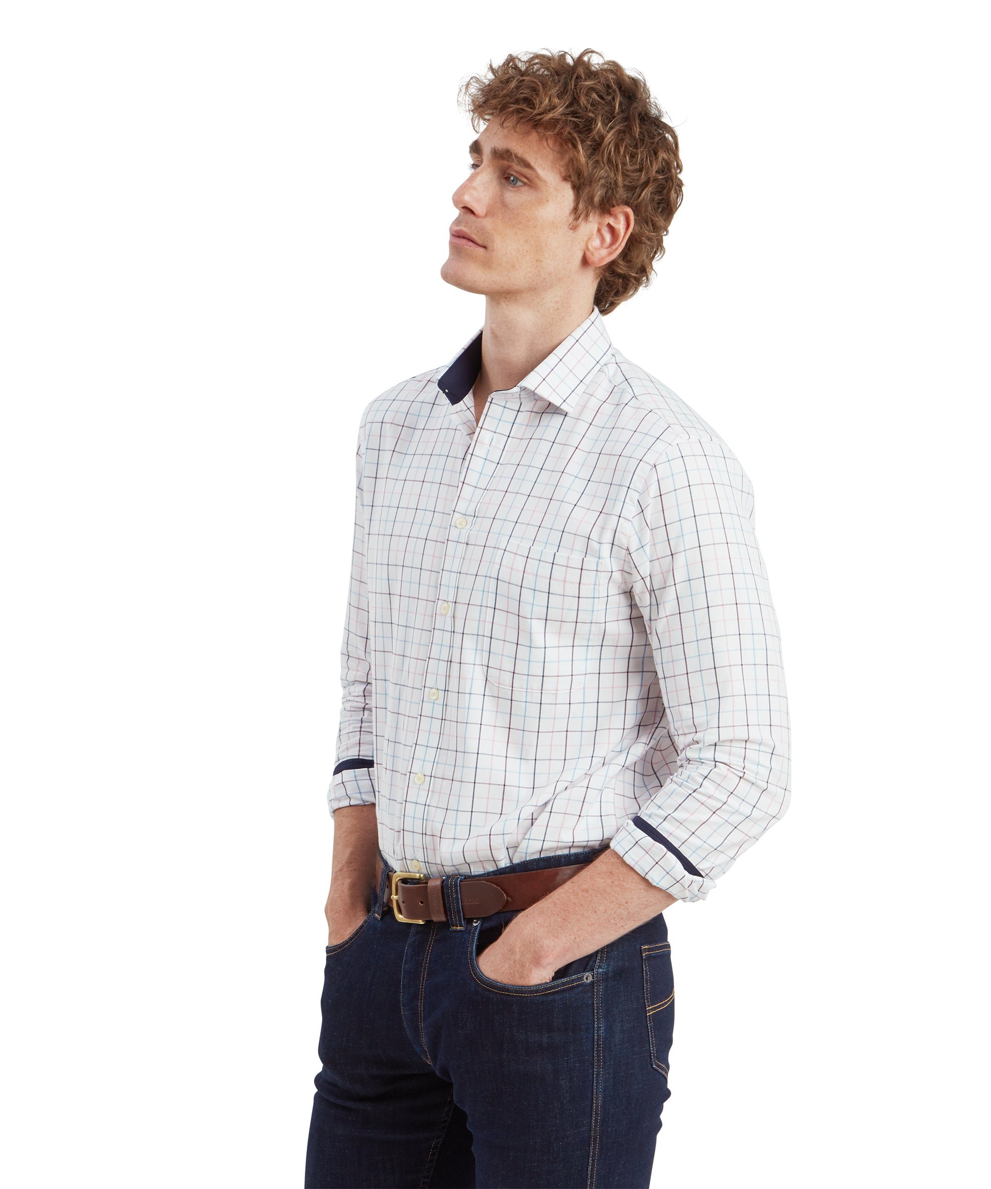 A side profile of the young man wearing the Schöffel Wells Tailored Shirt for Men in Red. His posture is relaxed, with both hands in his jeans pockets. The contrasting inner collar and cuff lining of the shirt in navy blue are subtly visible, adding a touch of sophistication to the overall look.