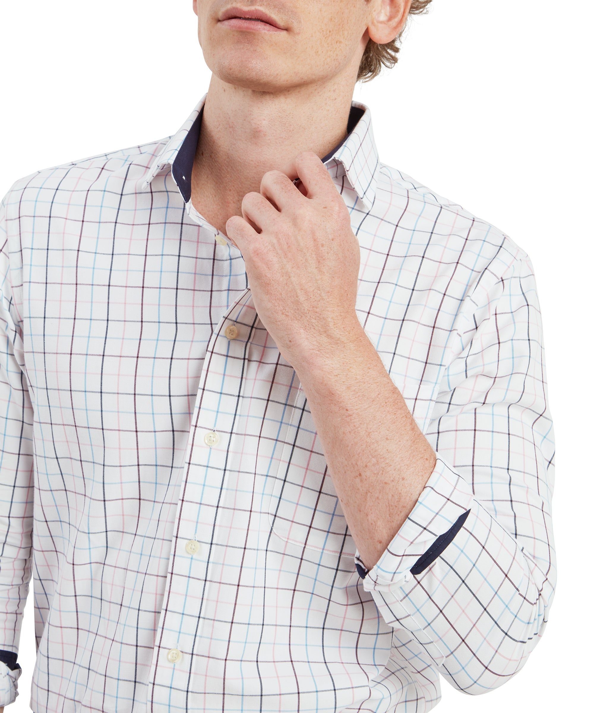 A close-up of the young man's upper body, focusing on the details of the Schöffel Wells Tailored Shirt for Men in Red's collar and button placket. The grid pattern of red, blue, and light brown lines is clearly visible, along with the navy blue contrast lining inside the collar. He is gently pulling the collar with his right hand, showcasing the shirt's premium craftsmanship and attention to detail.