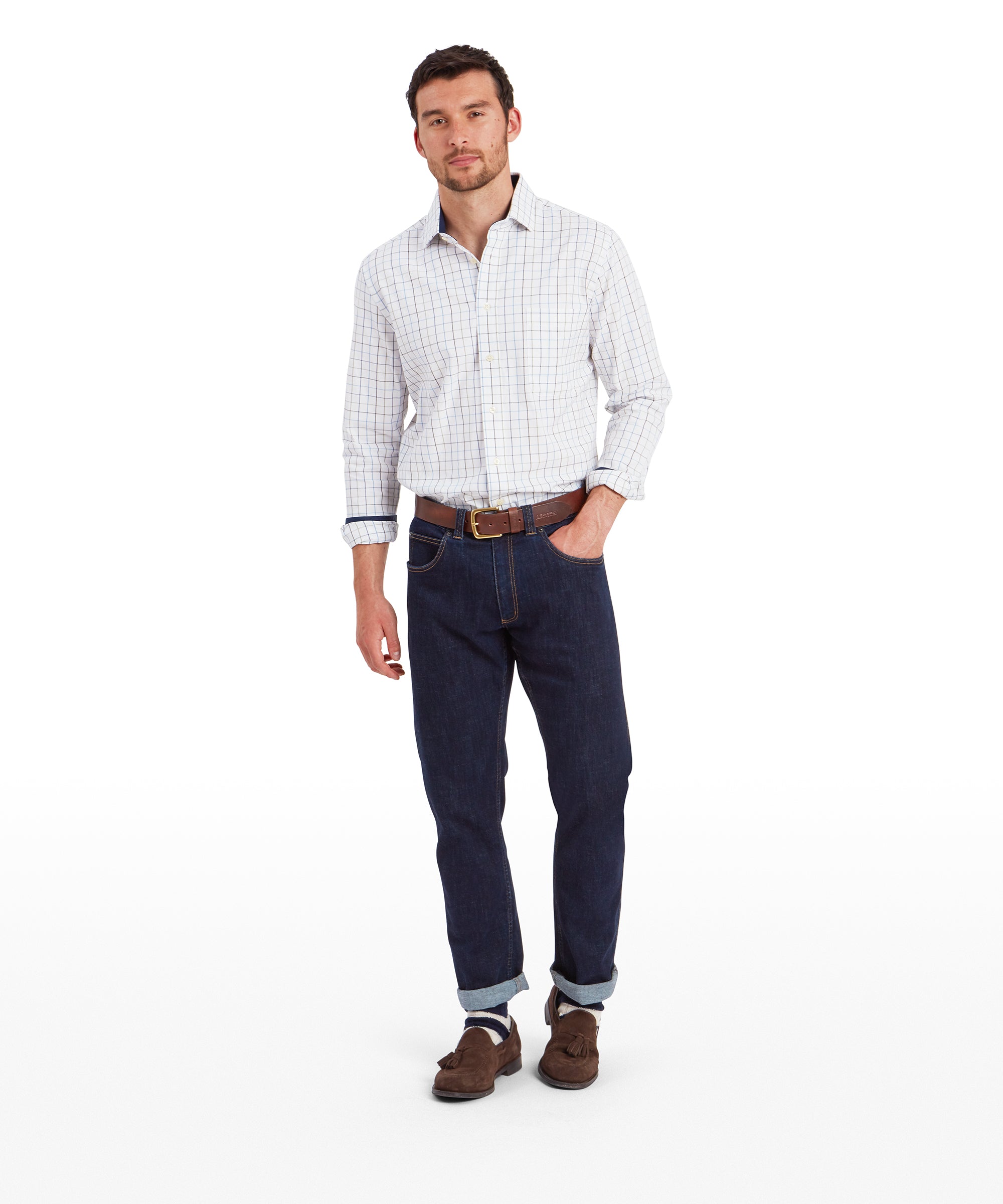 The man is standing in a relaxed posture, wearing the same Schöffel Wells Tailored Shirt for Men in Blue as in the first image. He pairs the shirt with dark blue jeans, brown suede loafers with tassels, and a brown leather belt. He is slightly turned to the side, giving a casual and approachable vibe.