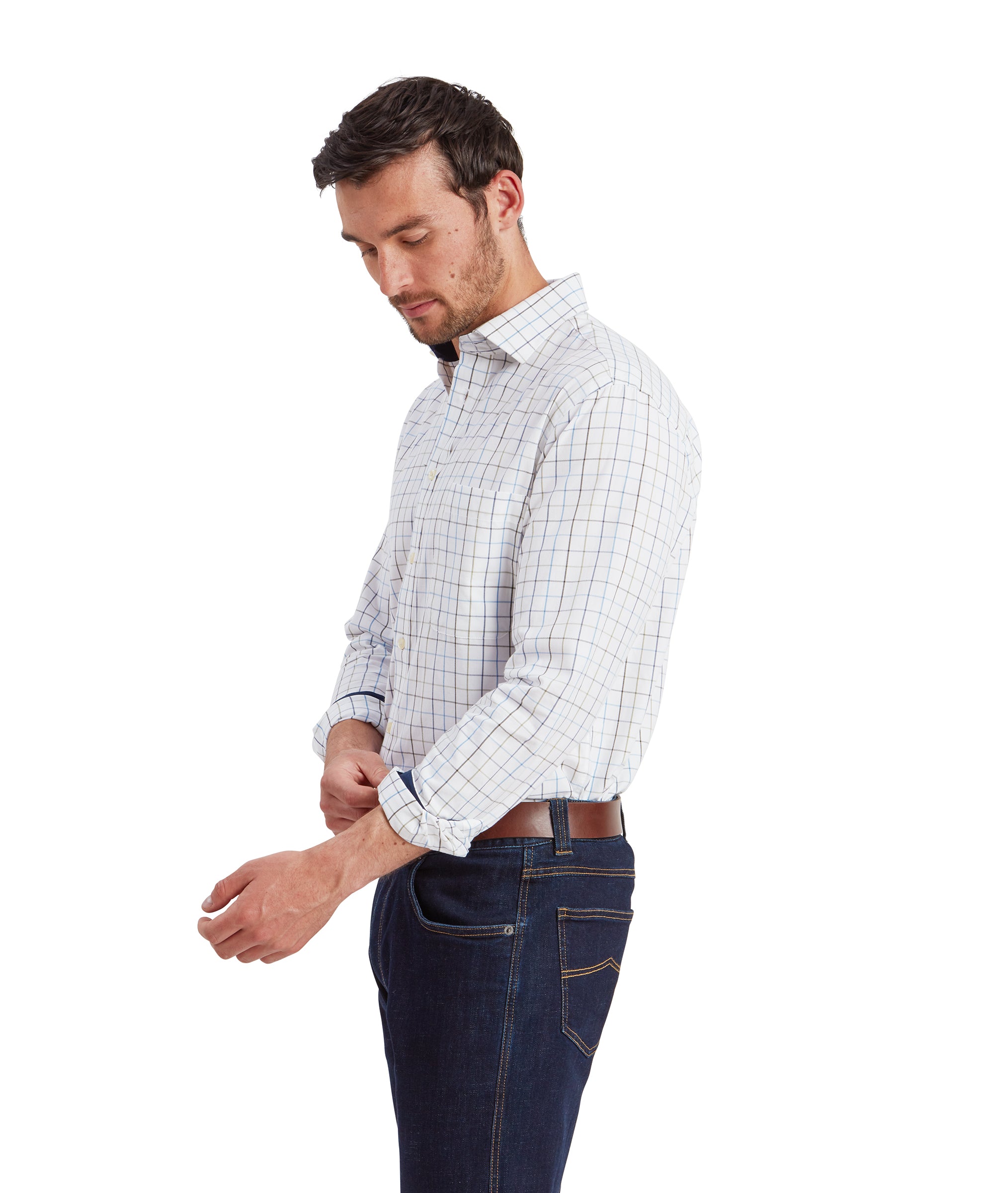 This image shows the man in the same Schöffel Wells Tailored Shirt for Men in Blue and jeans, with his head slightly tilted downward as he focuses on adjusting his sleeve. The side profile highlights the shirt's fit along the shoulder and arm, as well as the details of the checkered pattern.