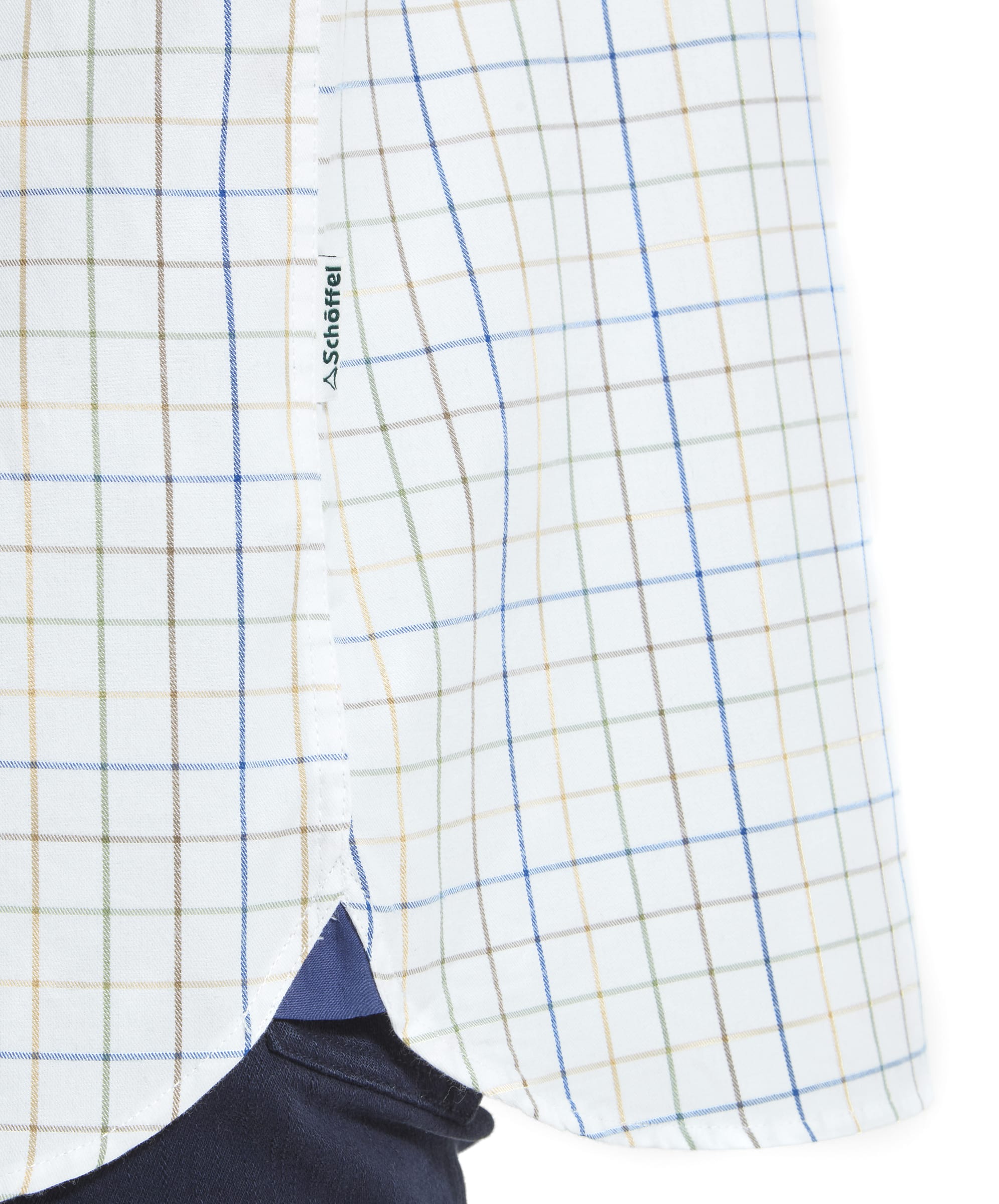 A detailed shot of the Schöffel Wells Tailored Shirt for Men in Green’s side hem, showing the curved finish with a small Schöffel brand label sewn into the seam. The same check pattern runs through the shirt, and the navy trousers provide a sharp contrast to the light colors of the shirt.