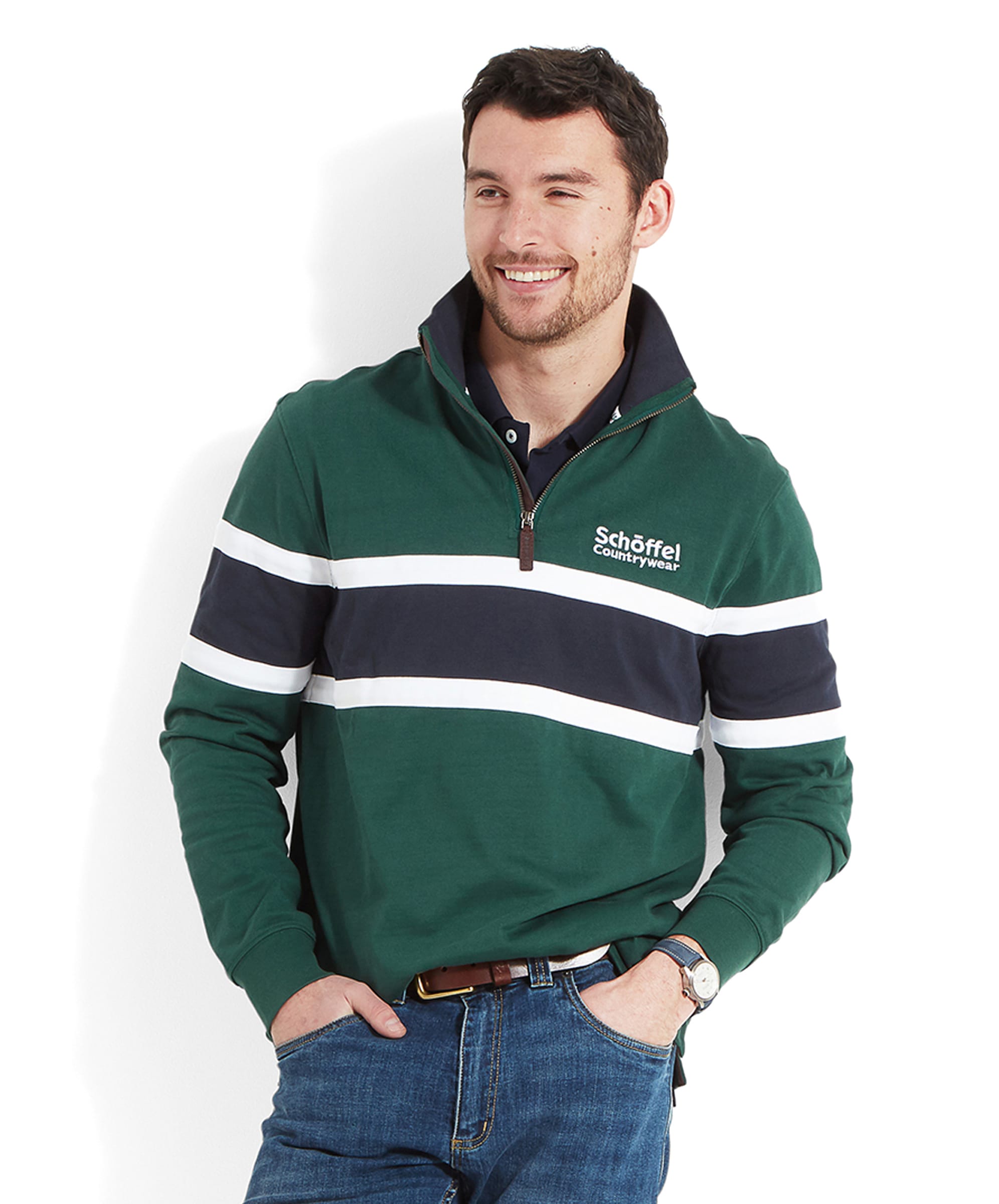 A man is smiling while wearing a Schöffel Exmouth Heritage 1/4 Zip for Unisex in Green with white and navy stripes and the Schoffel Countrywear logo, paired with blue jeans and a watch.