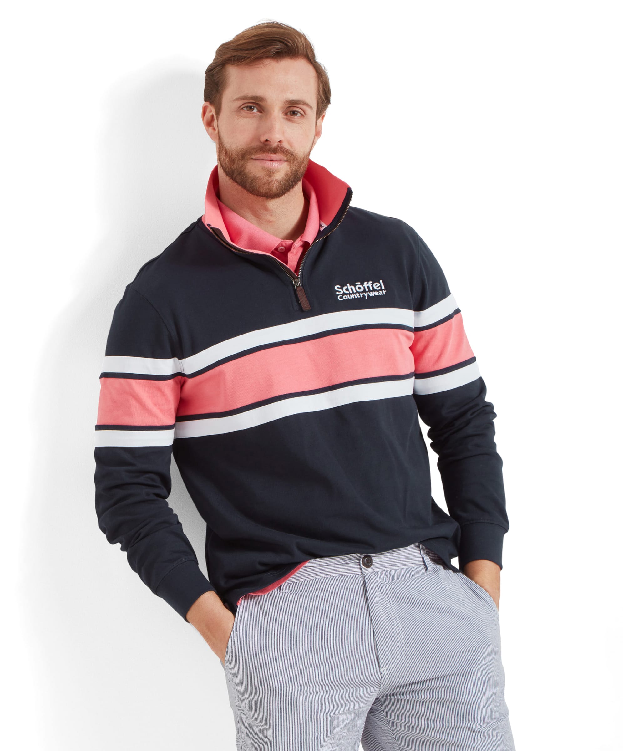 A man with a beard wearing a Schöffel Exmouth Heritage 1/4 Zip for Unisex in Navy with "Schöffel Countrywear" embroidered on the chest. He is standing against a white background with his hands in his pockets, smiling slightly.