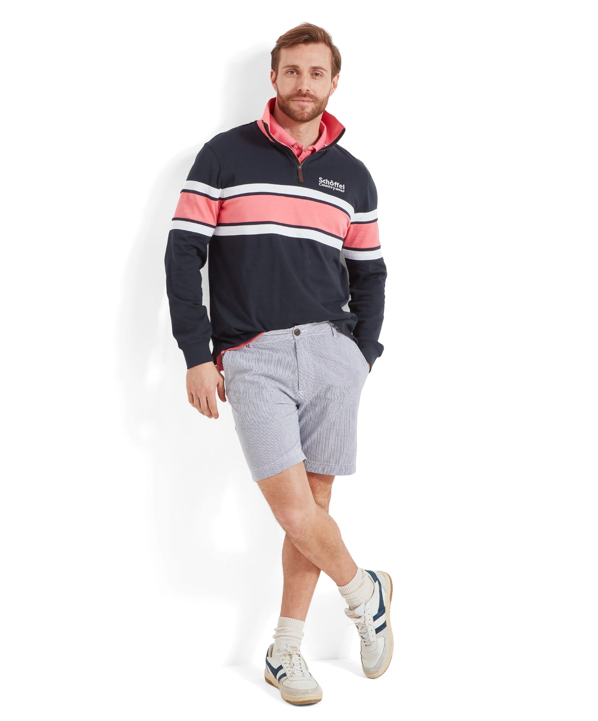 The same man wearing the Schöffel Exmouth Heritage 1/4 Zip for Unisex in Navy, paired with light blue striped shorts and white trainers. He is standing against a white background, with one leg crossed over the other.