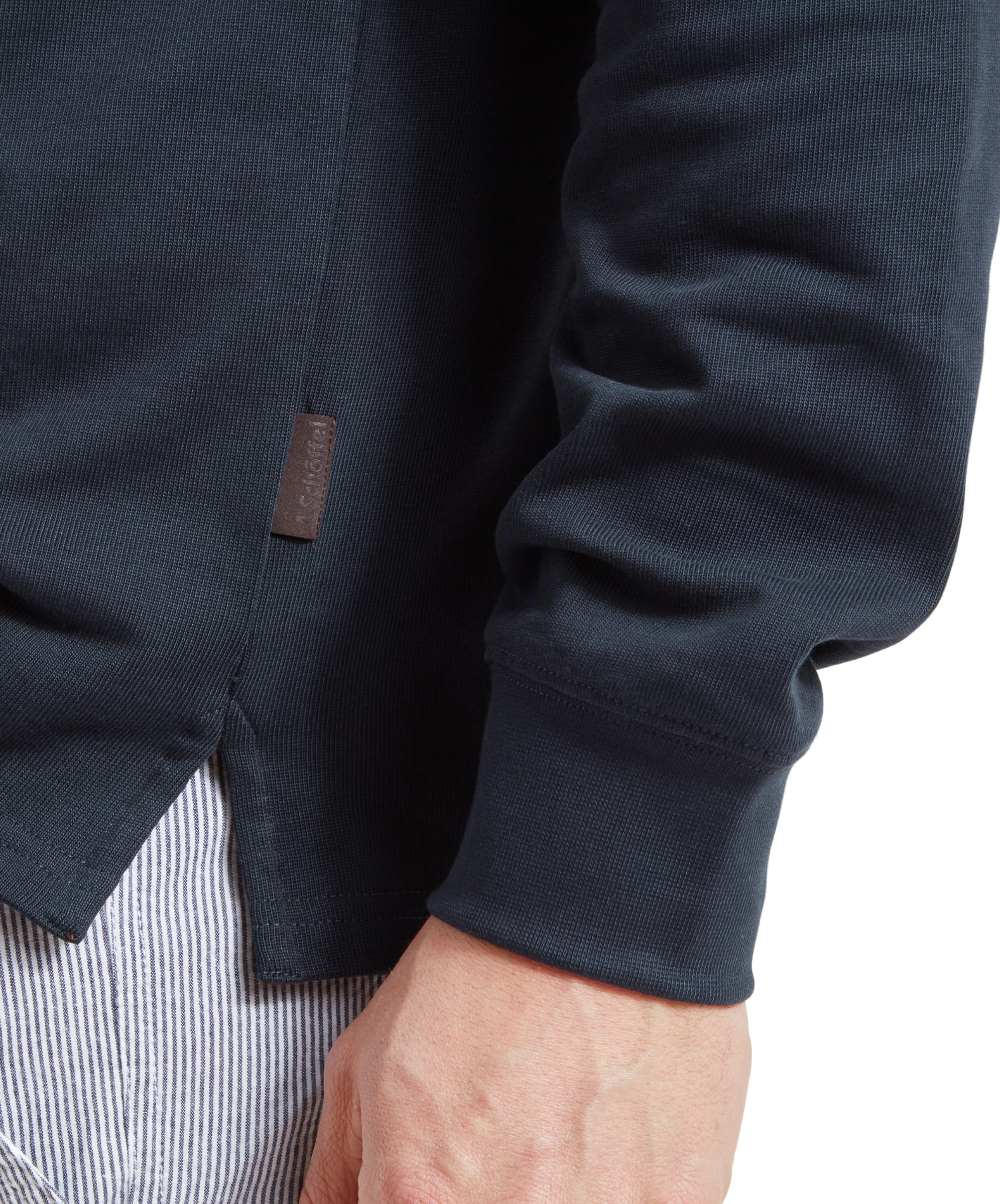 Close-up of the man's hand and lower part of the Schöffel Exmouth Heritage 1/4 Zip for Unisex in Navy, showing the brown Schöffel tag at the hem. The sweatshirt is navy with a ribbed cuff.