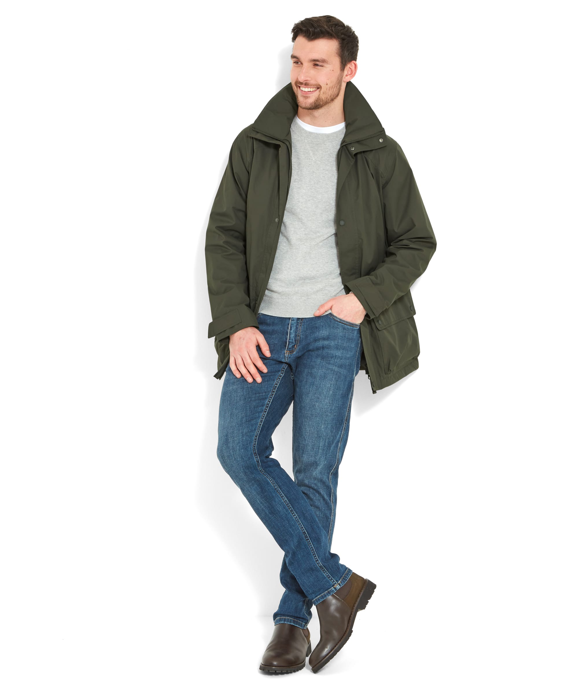 The man is smiling and standing casually with one leg crossed over the other while wearing the Schöffel Unisex Ketton Jacket II in Green, with the jacket slightly open revealing a grey sweater underneath.