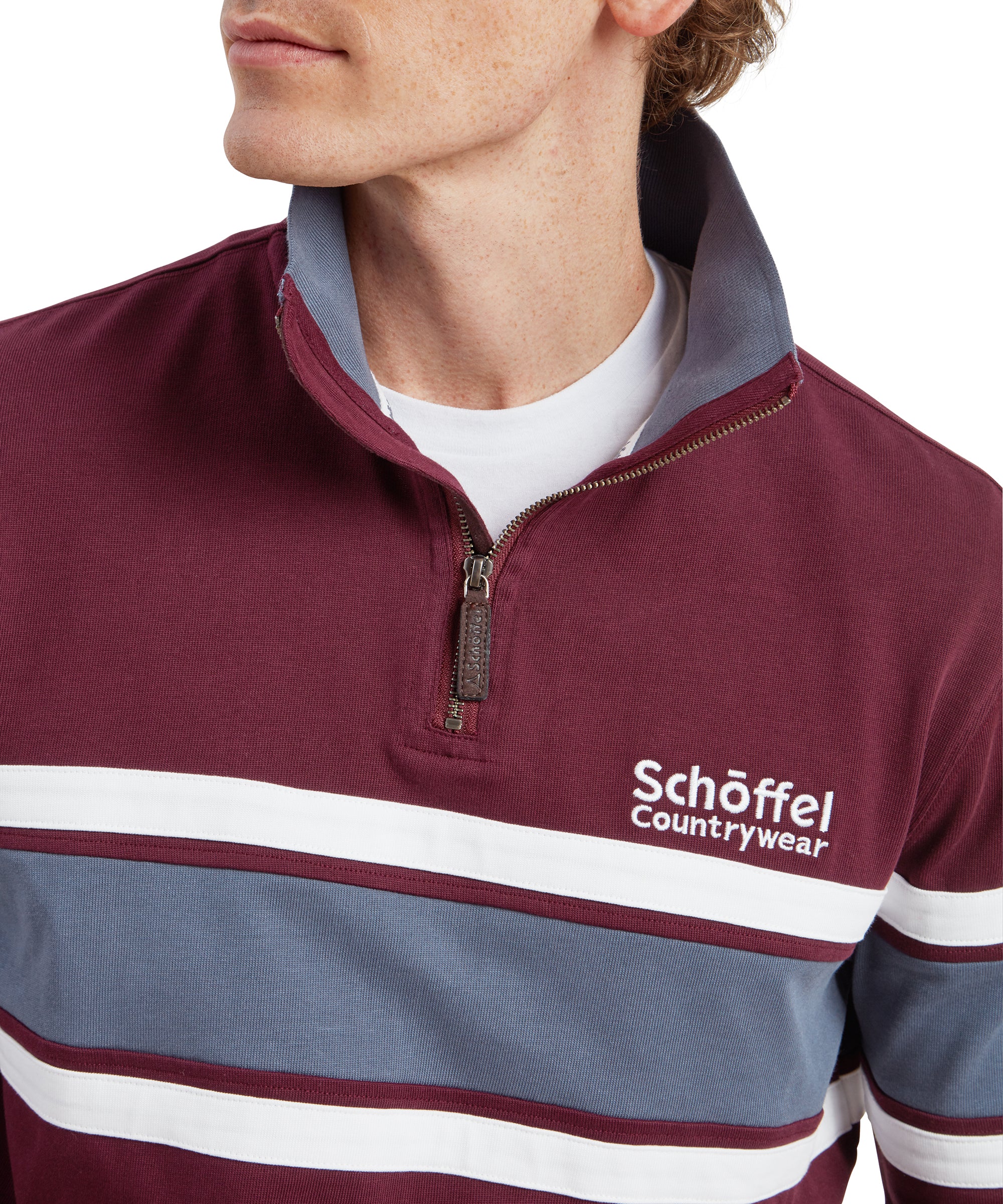 A close-up shot of the upper chest area of the Schöffel Exmouth Heritage 1/4 Zip for Unisex in Red, focusing on the collar and zipper. The "Schöffel Countrywear" logo is prominently embroidered on the left chest, and the collar reveals a contrasting light blue inner lining. The fabric appears to be soft and comfortable.