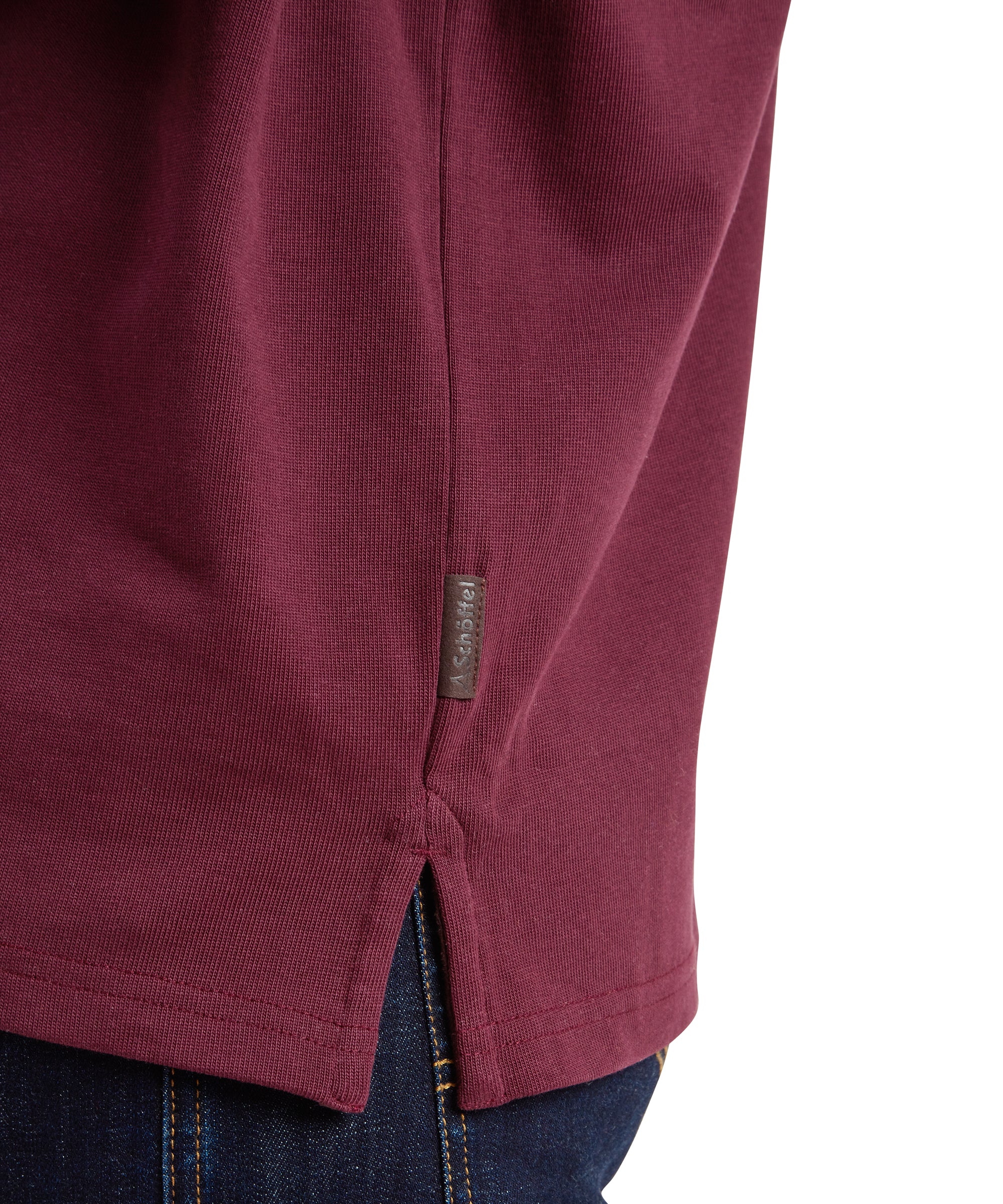 Close-up detail of the side hem of the Schöffel Exmouth Heritage 1/4 Zip for Unisex in Red, showcasing the small fabric tag with the Schöffel logo stitched near the hem on the side seam. The texture of the fabric and the quality of the stitching are highlighted.