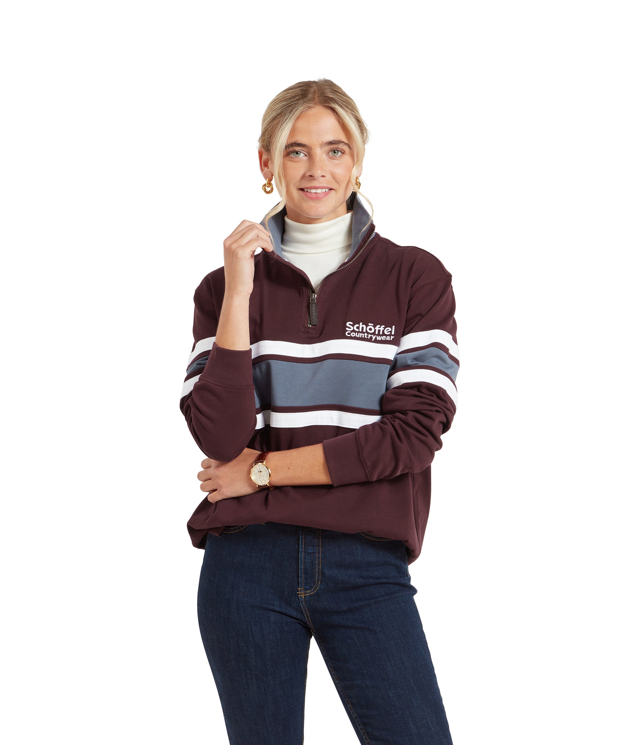 A woman wearing a Schöffel Exmouth Heritage 1/4 Zip for Unisex in Red with white and blue horizontal stripes. The pullover has the "Schöffel Countrywear" logo on the chest. She is posing with her arms crossed, wearing dark jeans, a white turtleneck underneath the pullover, gold hoop earrings, and a watch.