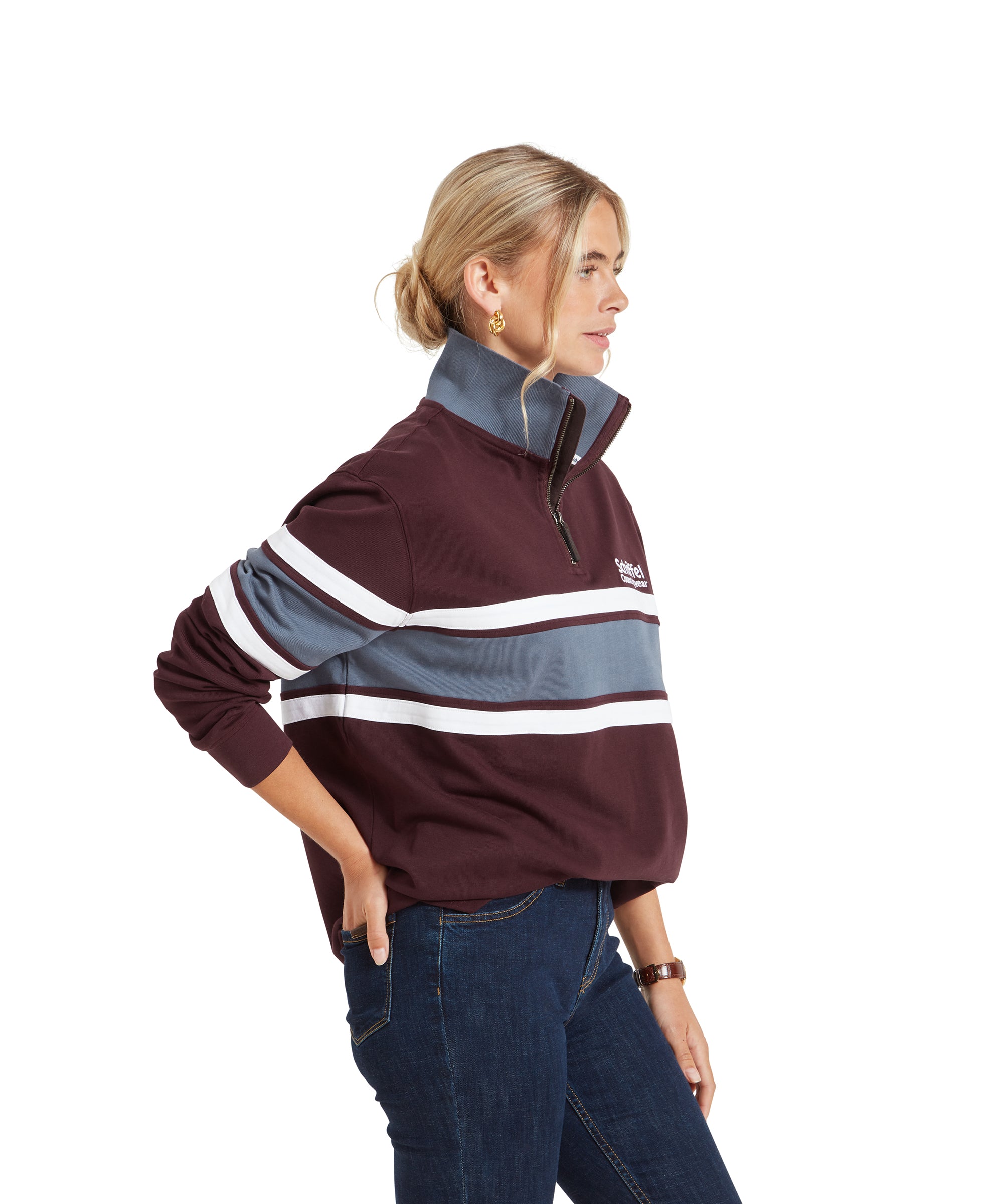 A side profile of the woman wearing the Schöffel Exmouth Heritage 1/4 Zip for Unisex in Red. She has her hand on her hip, highlighting the fit of the pullover. The blue collar contrasts with the maroon and white stripes on the body and sleeves.