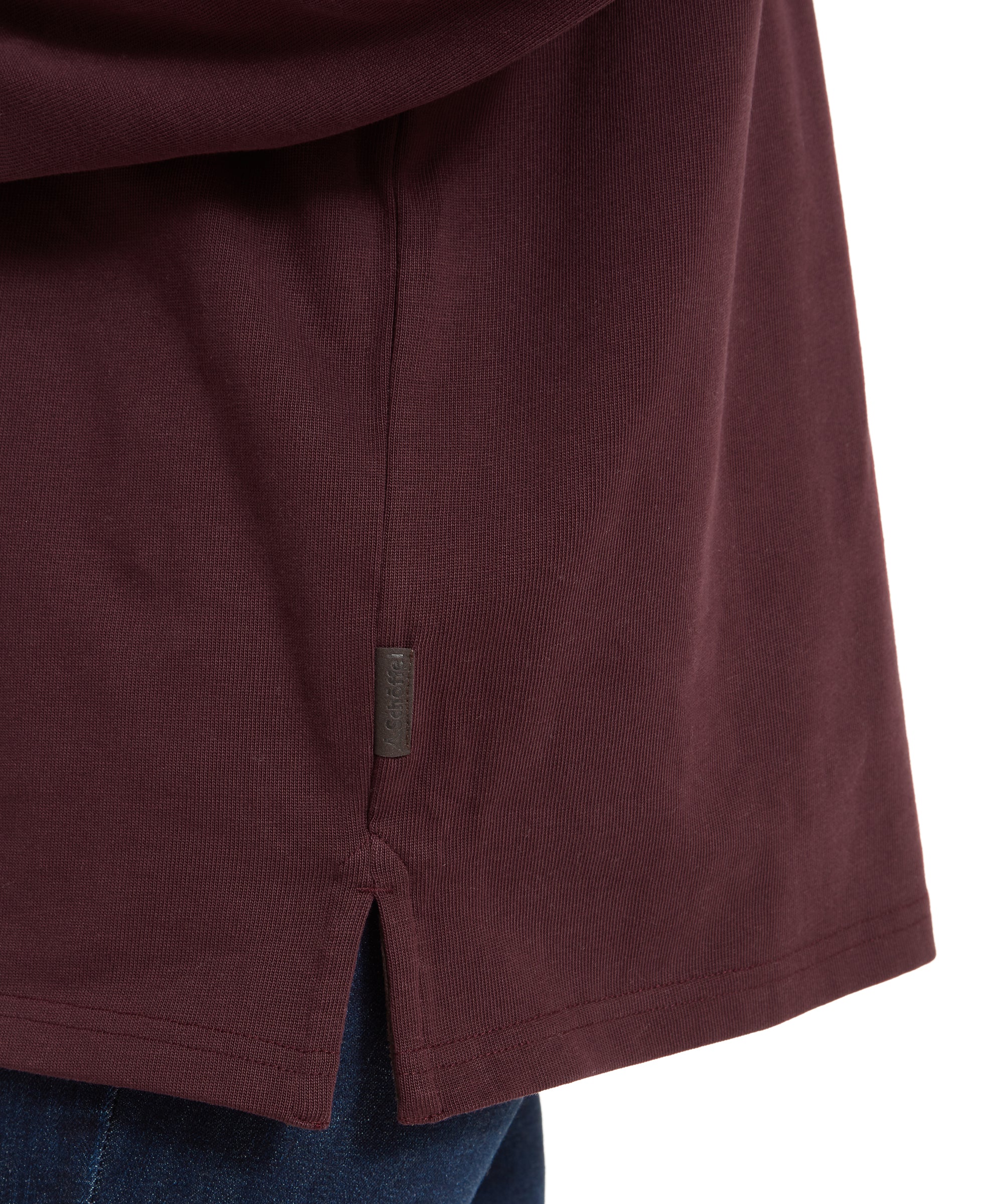 A close-up of the Schöffel Exmouth Heritage 1/4 Zip for Unisex in Red, focusing on the hem. A small tag with the Schöffel logo is visible near the side slit.