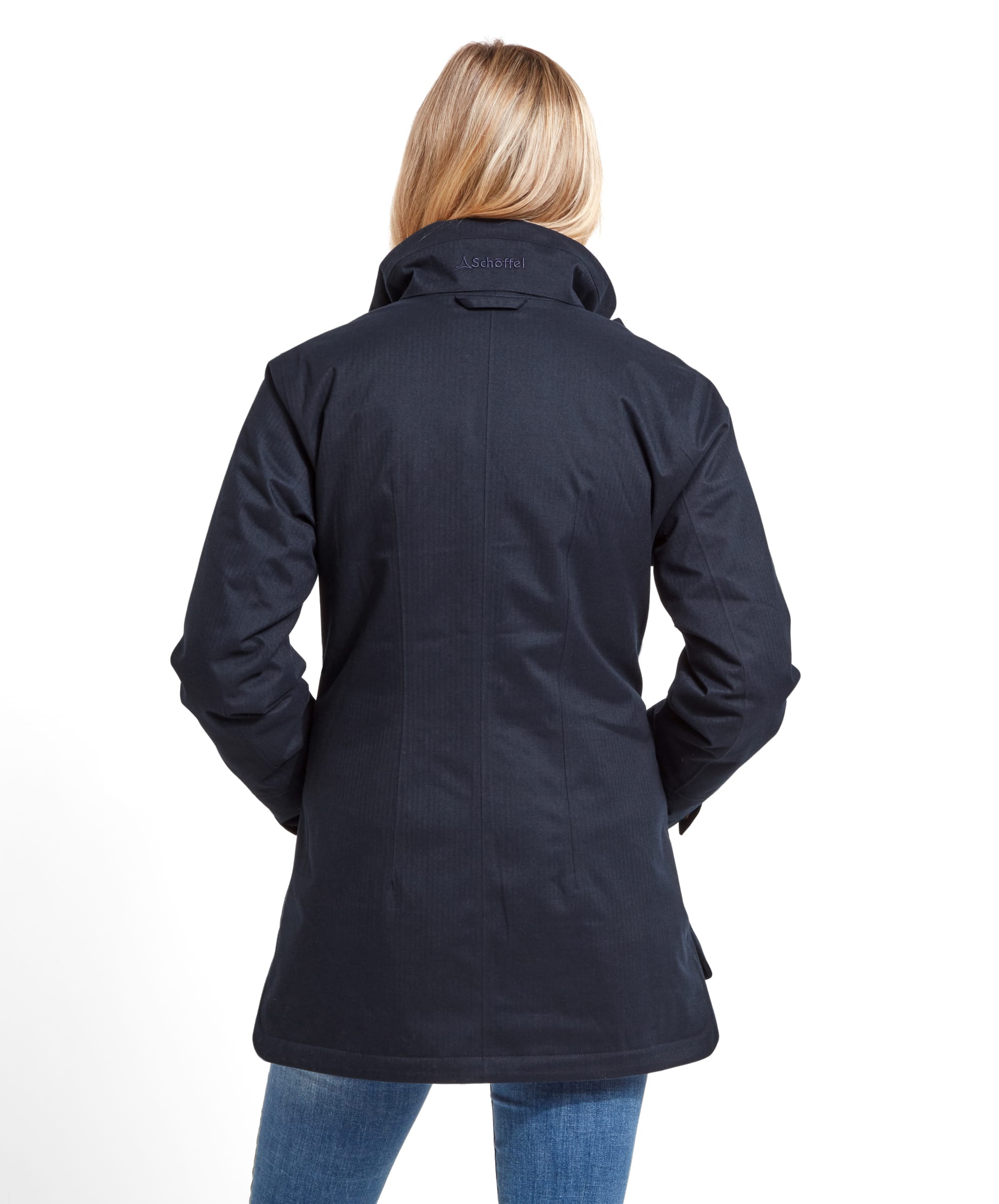 Rear view of the woman wearing the Schöffel Wakerley Jacket for Women in Blue, this time with the hood tucked in and only the jacket collar visible. The jacket’s tailored fit is emphasised, showcasing the woman’s waistline. The Schöffel logo is subtly embroidered on the back collar of the jacket.