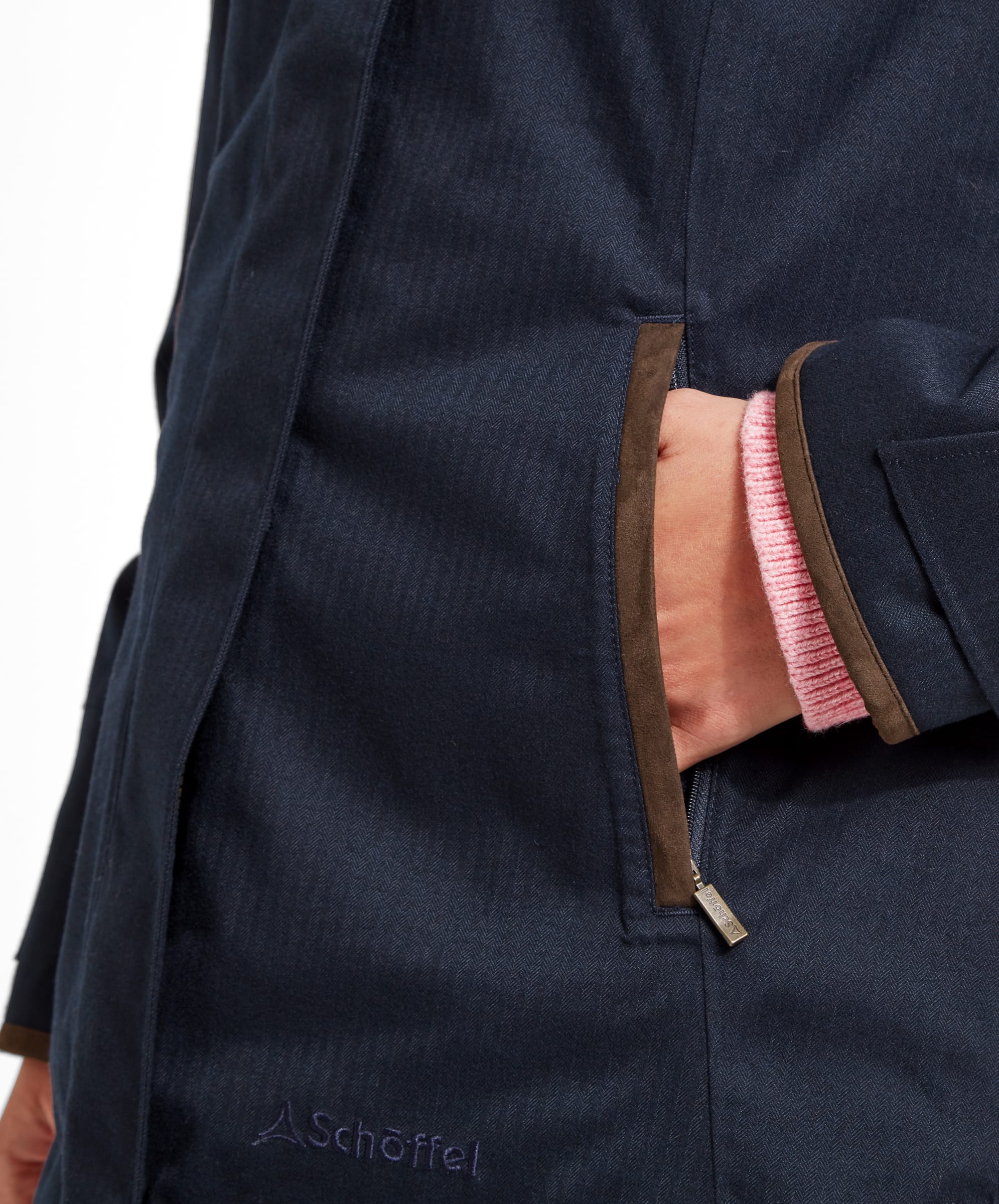 A close-up of the woman’s hand resting in the pocket of the Schöffel Wakerley Jacket for Women in Blue. The jacket's pocket is accented with brown trim, which matches the other brown details on the jacket. The woman's pink sweater sleeve peeks out from the jacket cuff, adding a touch of colour to the otherwise dark palette.