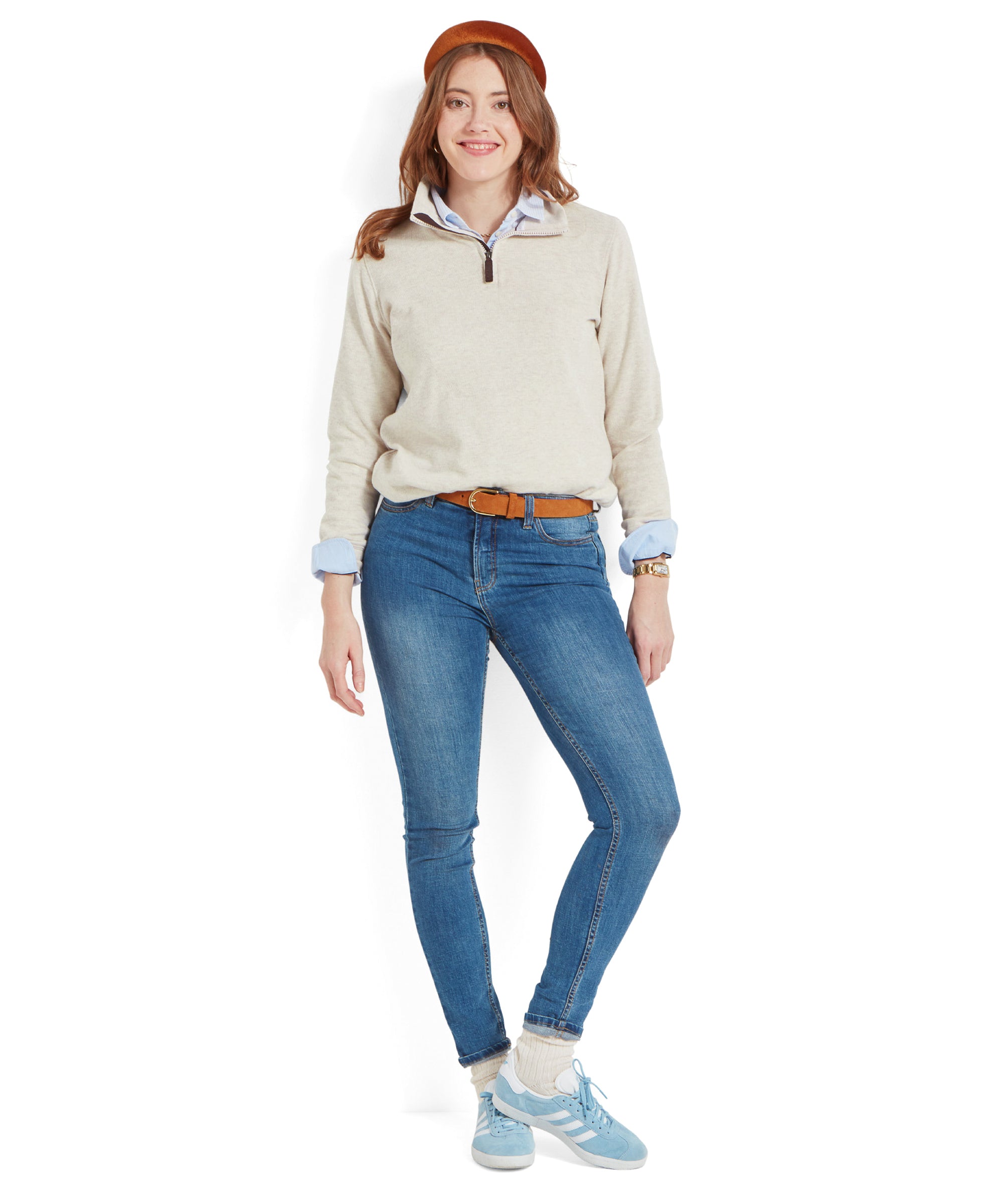 A model wearing a Schöffel Appletree Bay 1/4 Zip for Women in Light Brown over a blue collared shirt, blue jeans, a brown belt, a brown headband, and light blue trainers, standing and smiling.