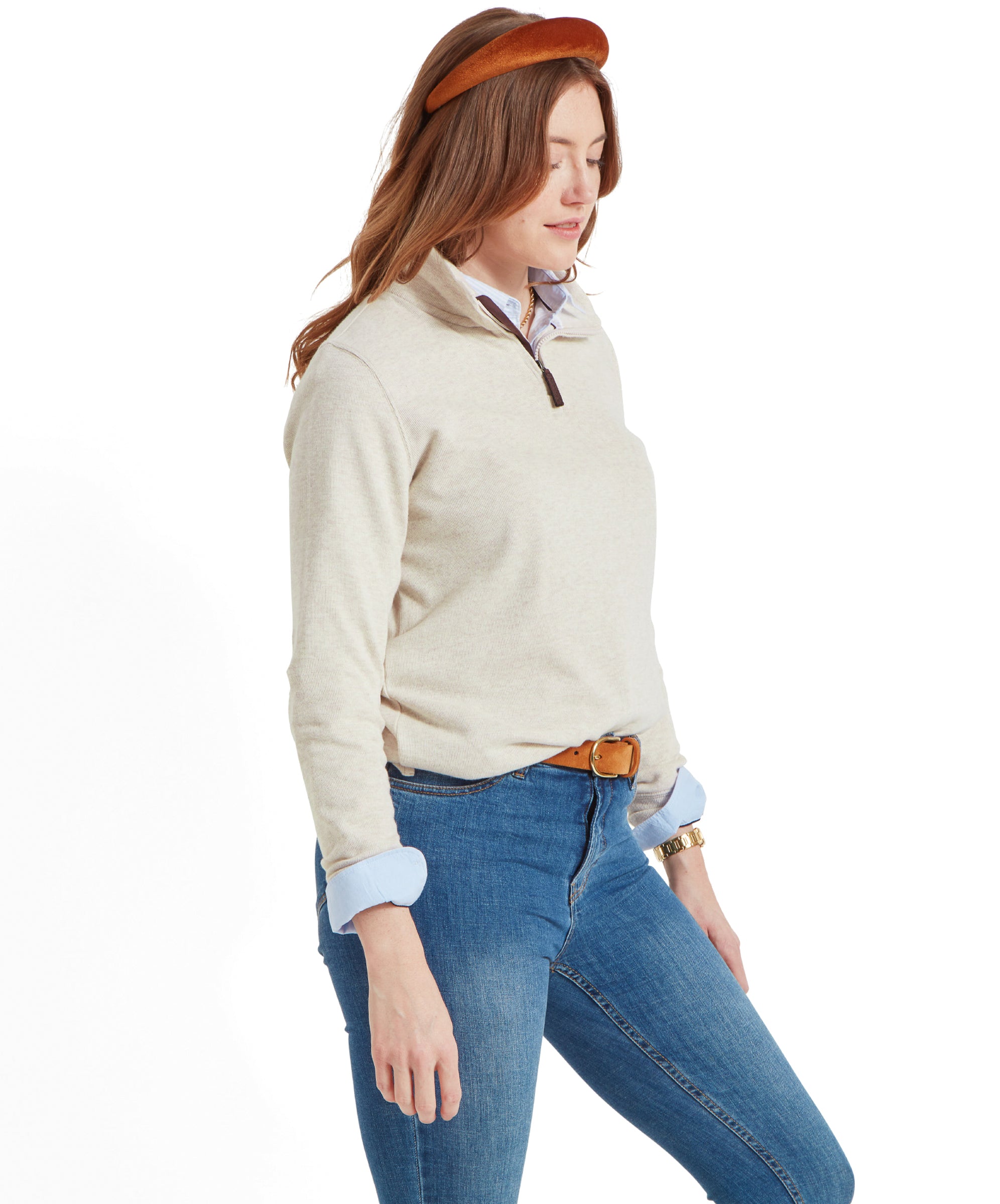 A model wearing a Schöffel Appletree Bay 1/4 Zip for Women in Light Brown over a blue collared shirt, blue jeans, a brown belt, and a brown headband, looking down.