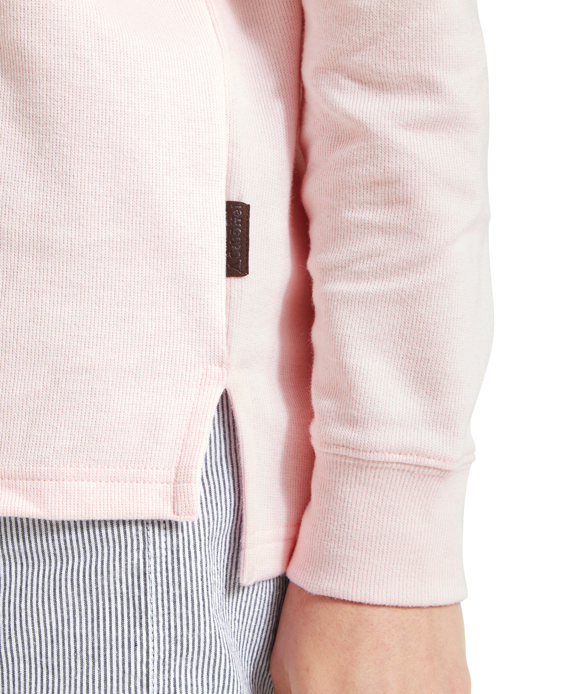 Close-up of a Schöffel Appletree Bay 1/4 Zip for Women in Pink hem with a brown tag, light blue striped shorts, and part of a model's hand.