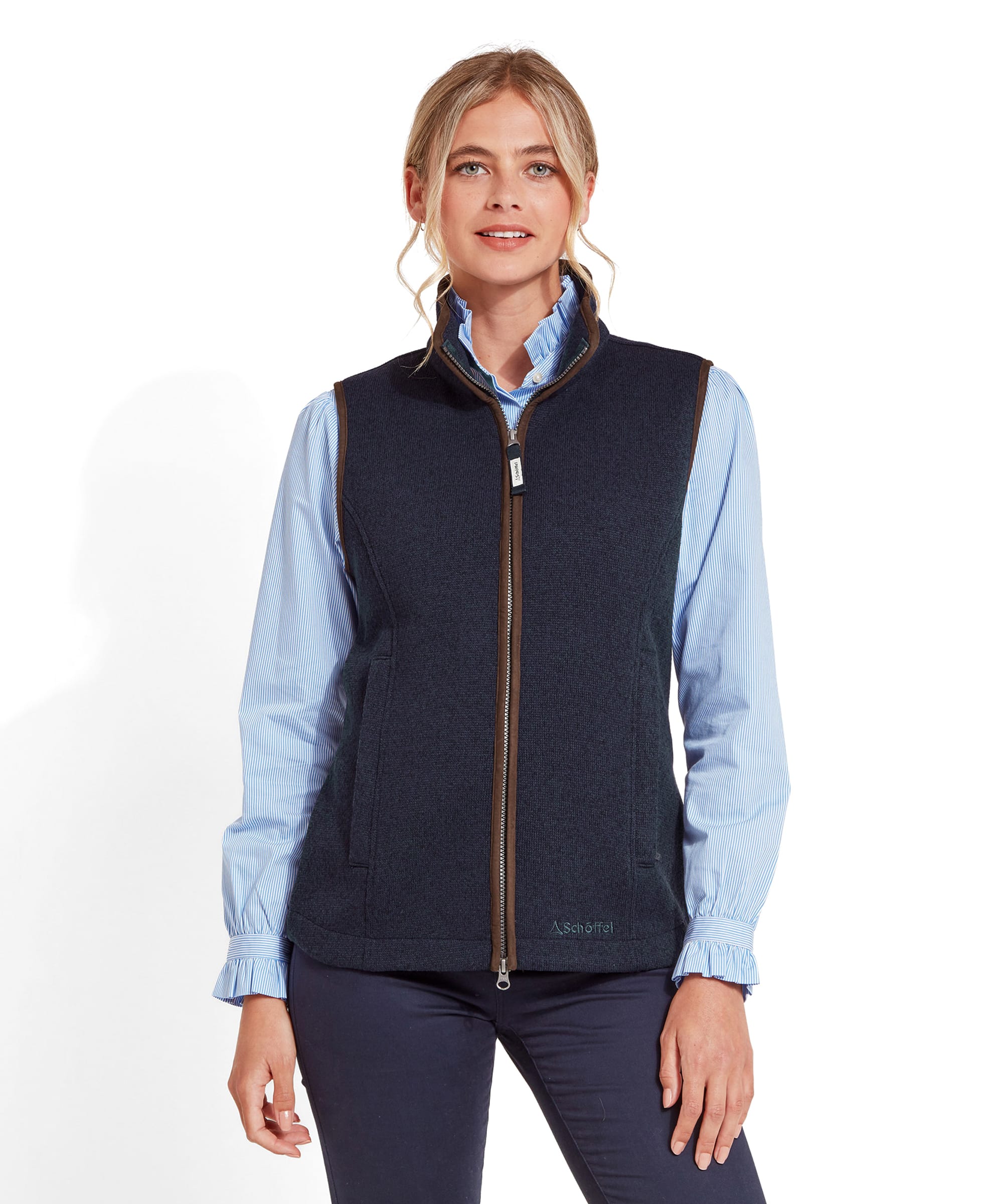 A woman wearing a Schöffel Ashton Gilet for Women in Blue over a light blue striped blouse. The gilet has a full zipper down the front and a high collar.