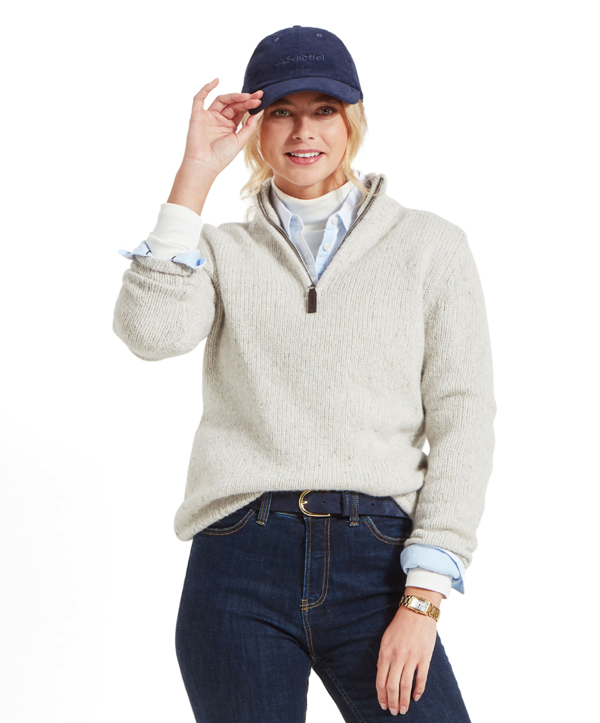 A woman wearing a Schöffel Women's Aviemore Alpaca Mix 1/4 Zip Jumper for Women in Cream, navy cap, and dark jeans, smiling and adjusting her cap.