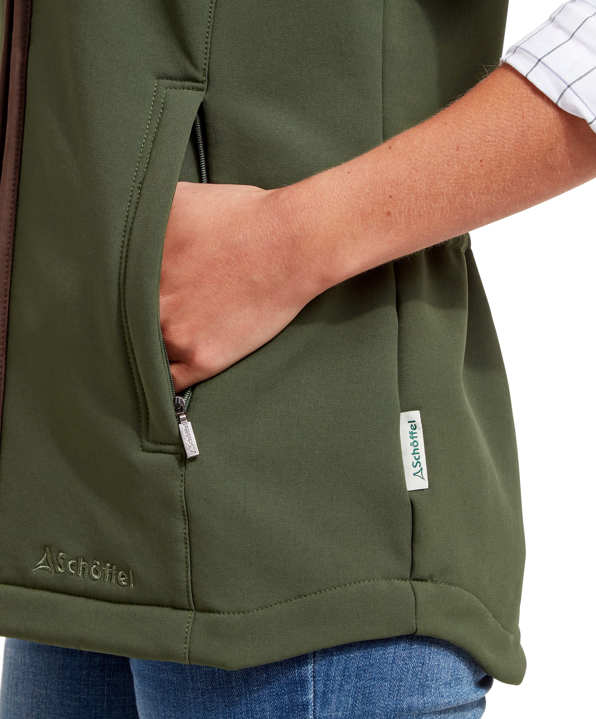 A close-up shot of the woman’s hand in the pocket of the Schöffel Belton Gilet for Women in Green, showing the Schöffel logo embroidered near the bottom hem of the gilet.