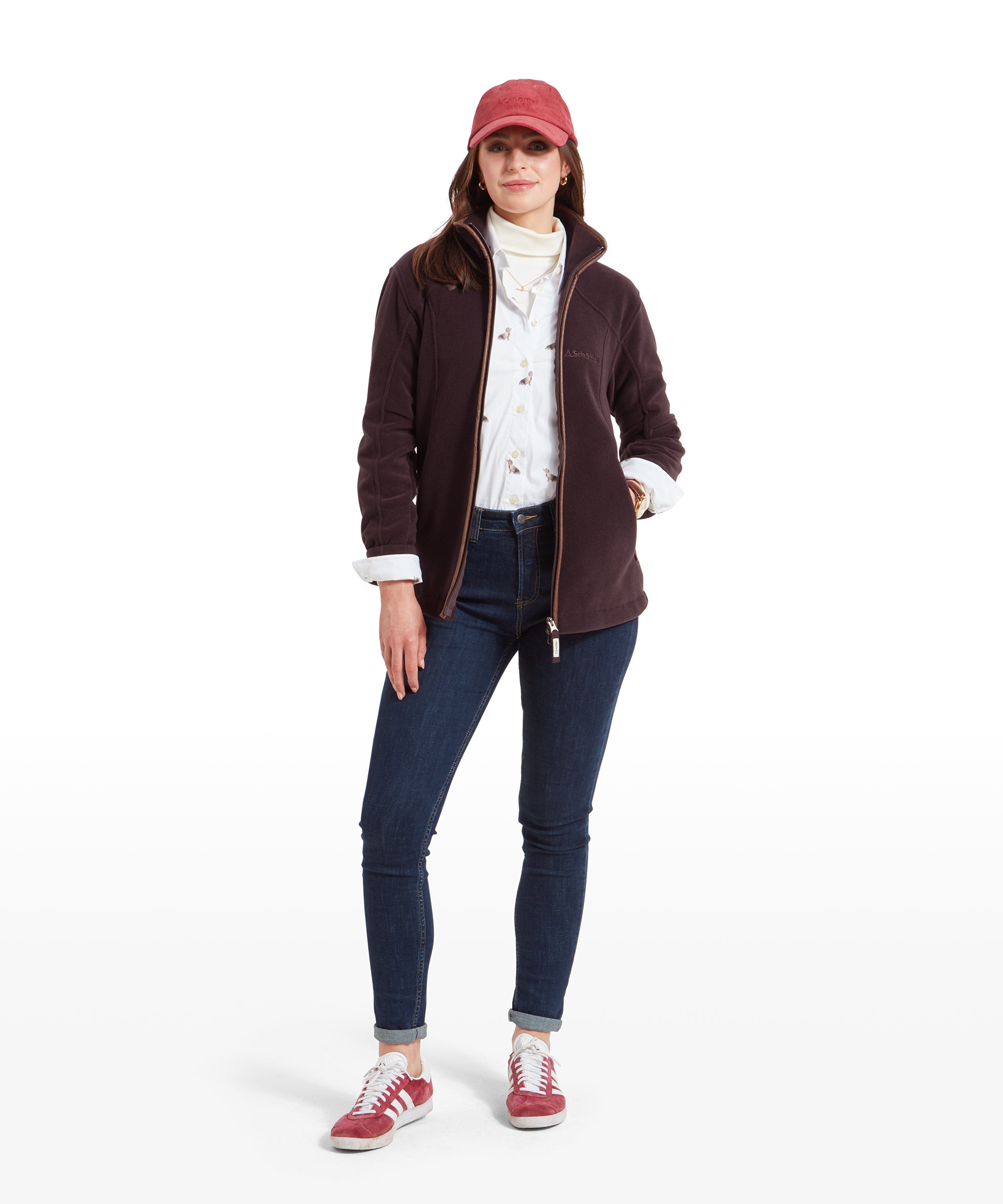 The same woman wearing the Schöffel Burley Fleece Jacket for Women in Purple and red cap, standing in a full-body shot. She is paired with dark jeans and red trainers, giving a casual and sporty look.