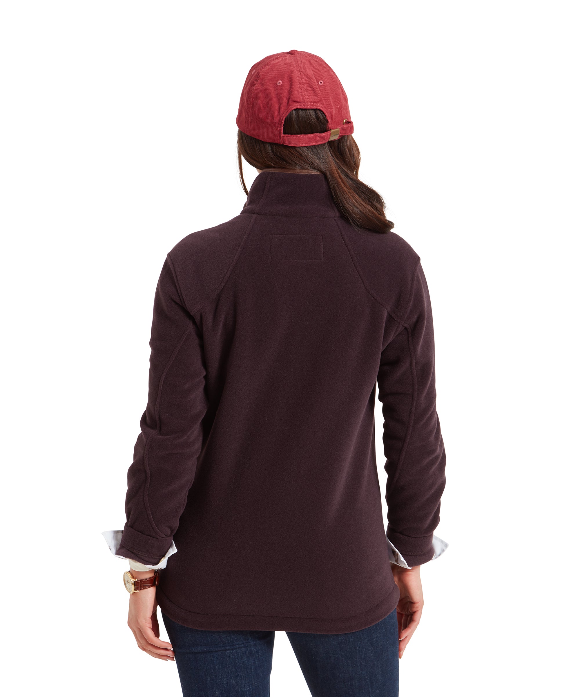 The woman is shown from behind, highlighting the back of the Schöffel Burley Fleece Jacket for Women in Purple and the red cap. The jacket has a slightly fitted look at the waist, and her hair is partially visible under the cap.