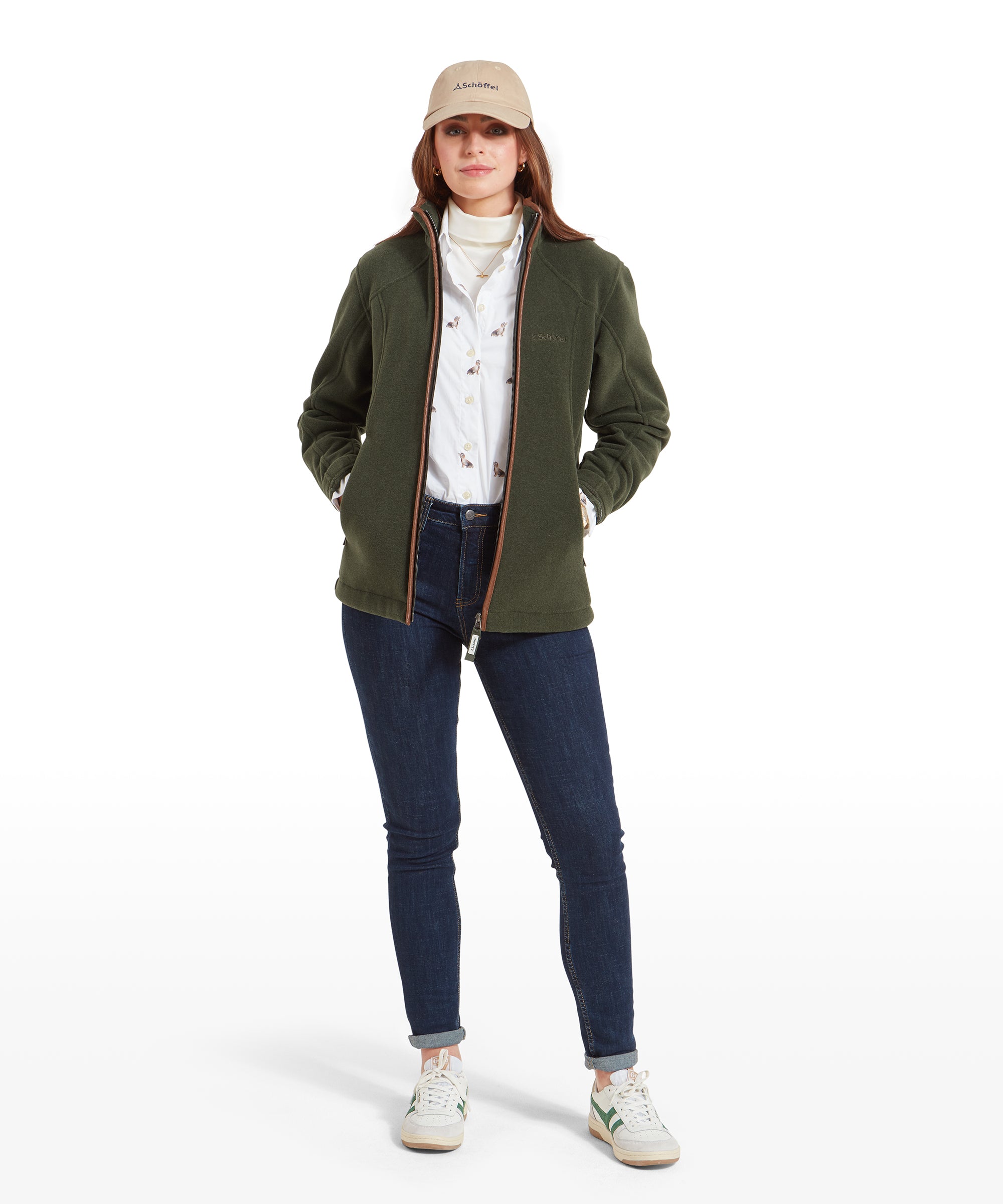 The same woman is standing fully, showcasing the Schöffel Burley Fleece Jacket for Women in Green, dark jeans, and white trainers. The jacket is zipped up fully, and she has her hands in the jacket's pockets.