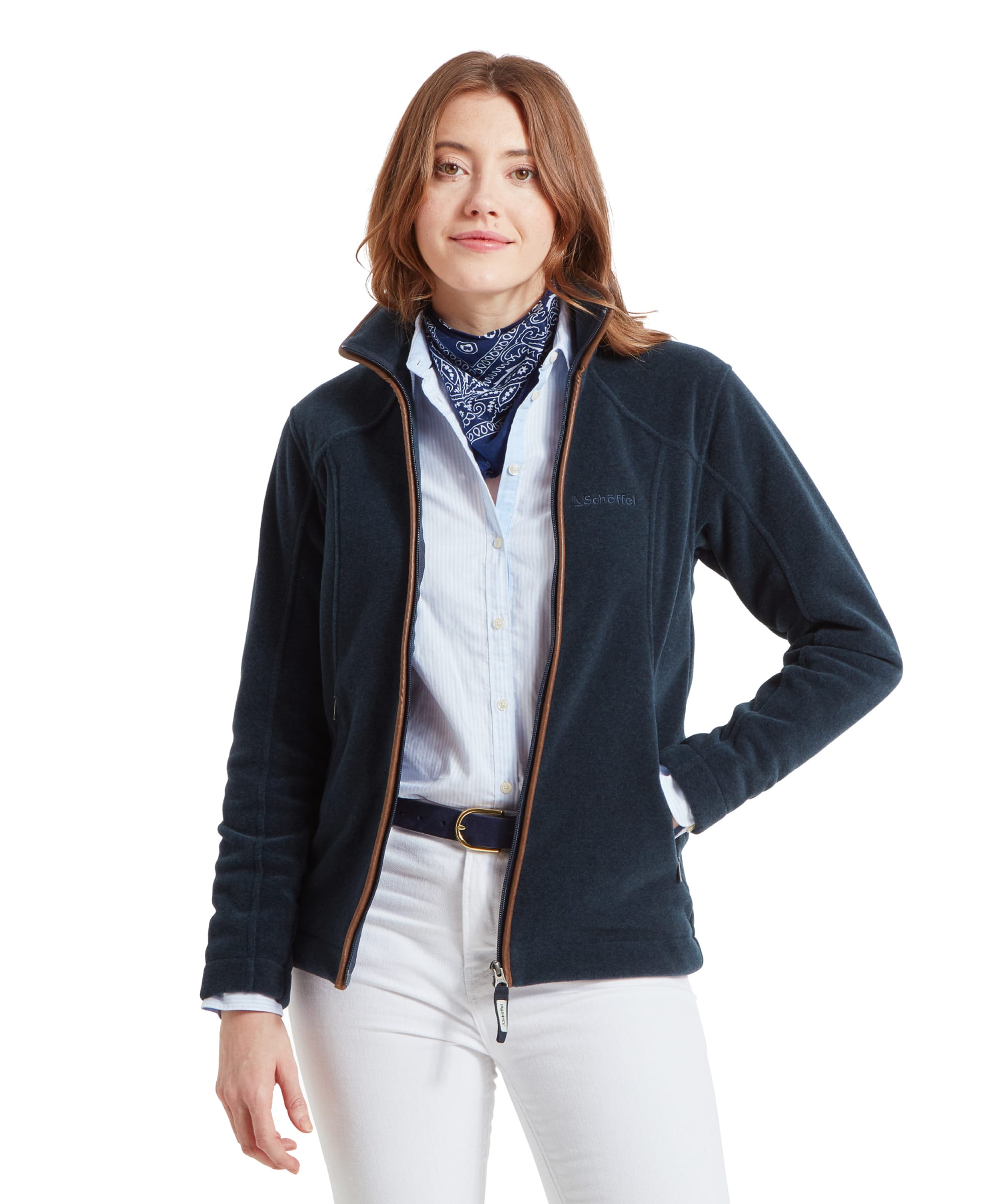 A woman wearing a Schöffel Burley Fleece Jacket for Women in Blue with a high collar, standing confidently with her hands in her pockets. She is accessorised with a blue and white patterned scarf and a light blue shirt underneath.