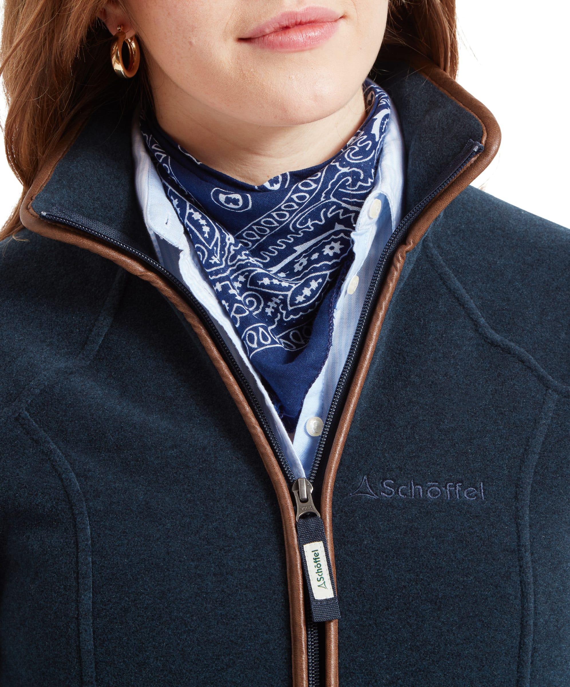 Close-up of the Schöffel Burley Fleece Jacket for Women in Blue’s front zip, highlighting the Schöffel logo on the zipper pull and the brown leather trim along the collar, with a glimpse of the blue and white scarf underneath.