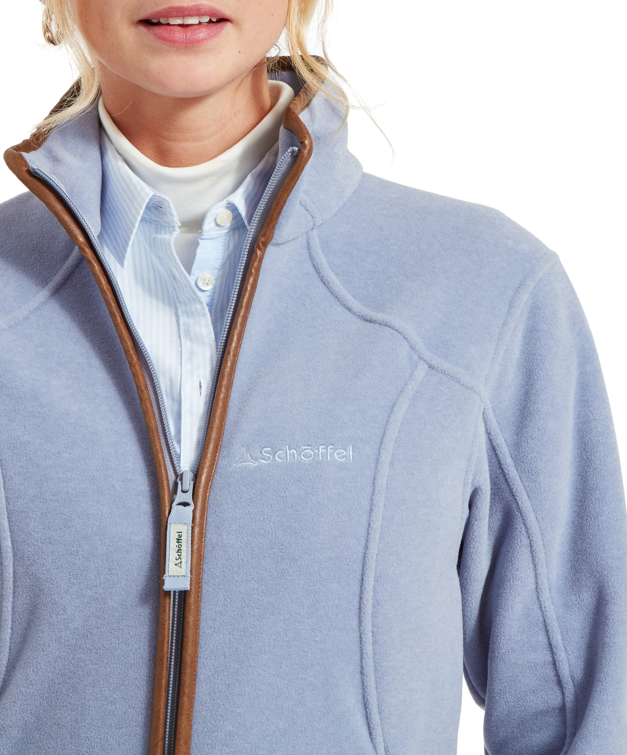 Close-up of a woman wearing a Schöffel Burley Fleece Jacket for Women in Light Blue, highlighting the embroidered Schöffel logo on the chest and the zippered front with leather trim. She is dressed in a blue button-up shirt and light brown belt.