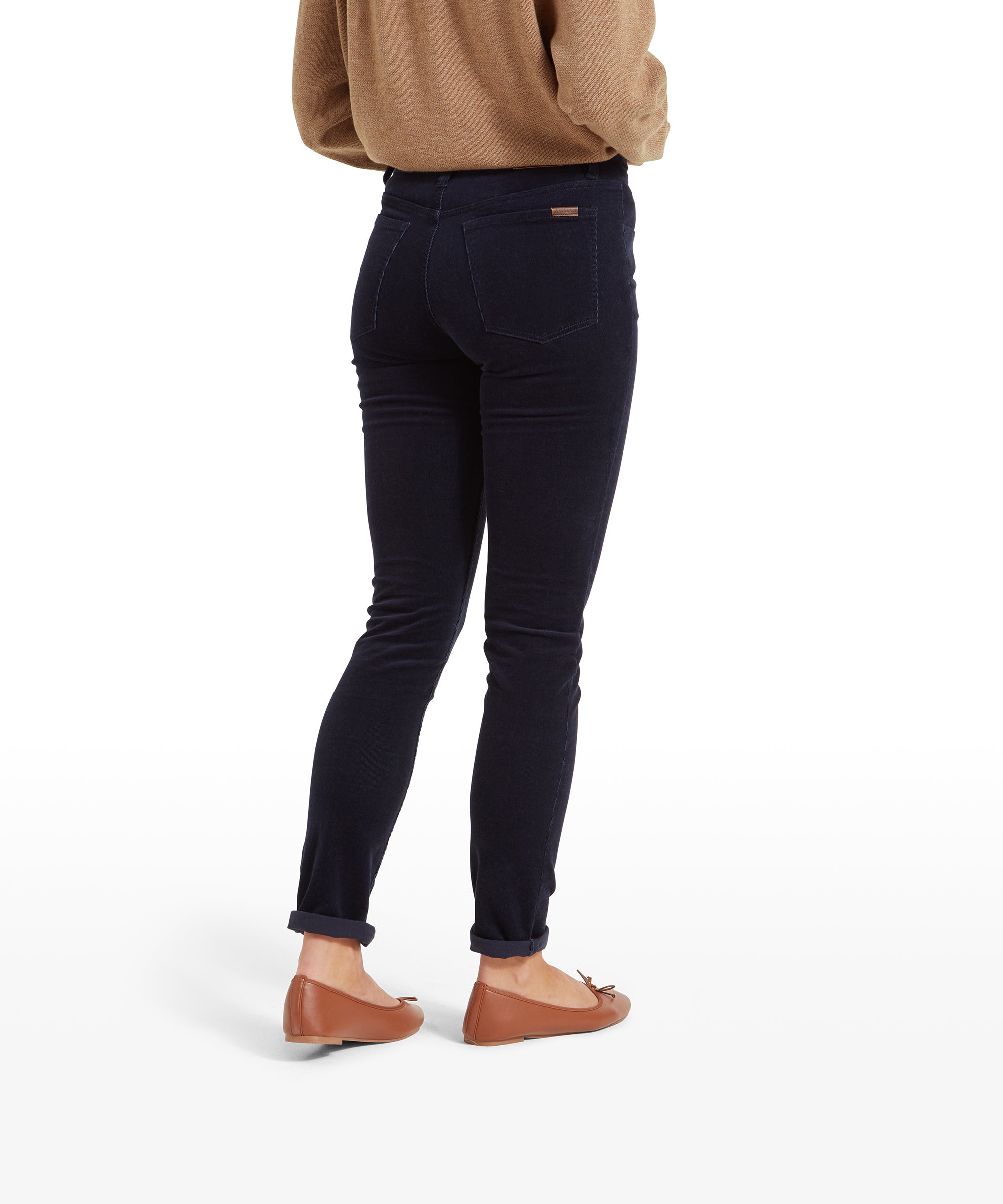 A back view of a woman wearing Schöffel Clover Cord Jean for Womens in Navy paired with a beige sweater. The jeans have a close fit with visible back pockets.