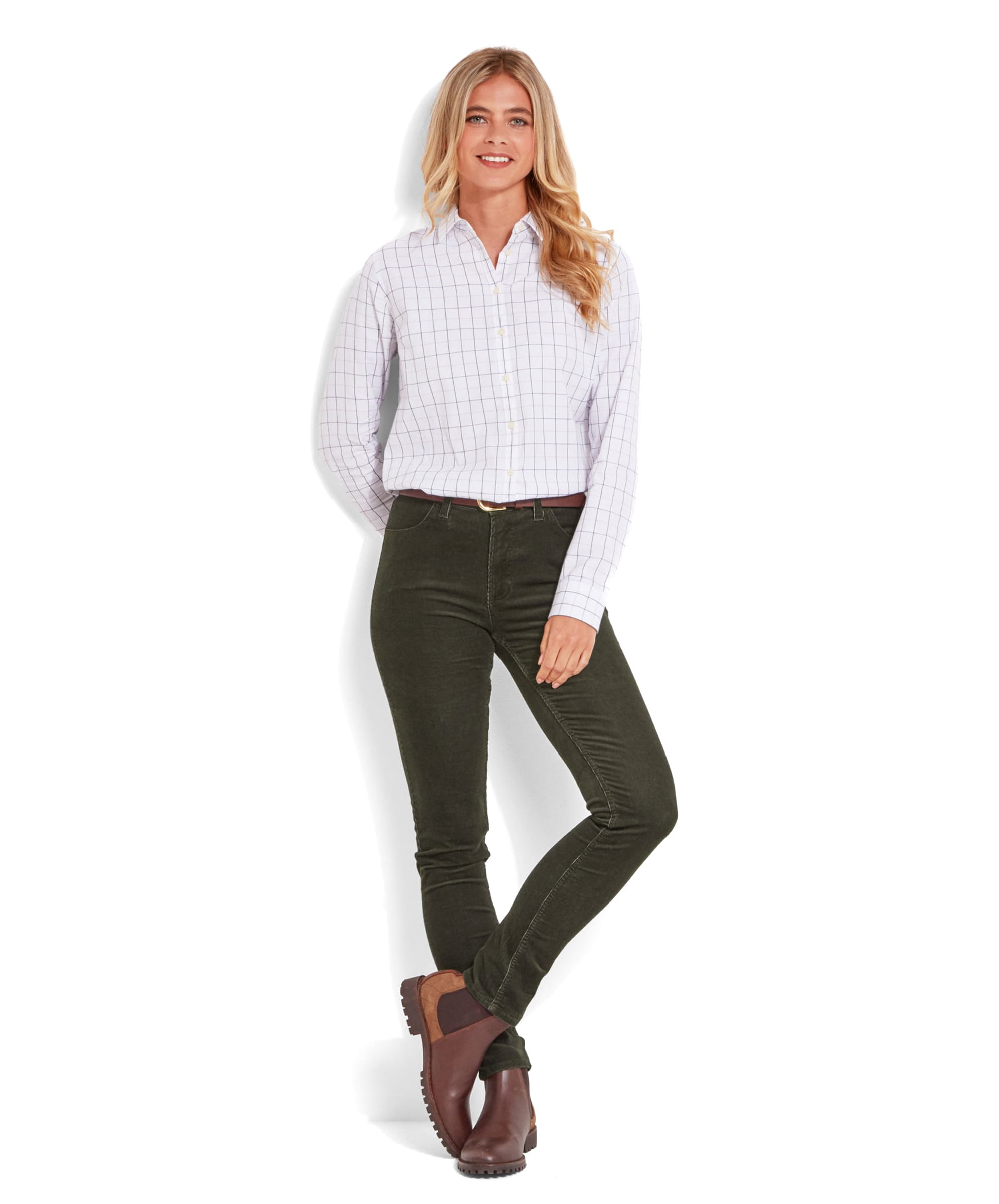 A full-body shot of a model wearing Schöffel Clover Cord Jean for Womens in Green, a white checked shirt, and brown Chelsea boots. The model is standing against a white background with one hand in her pocket.