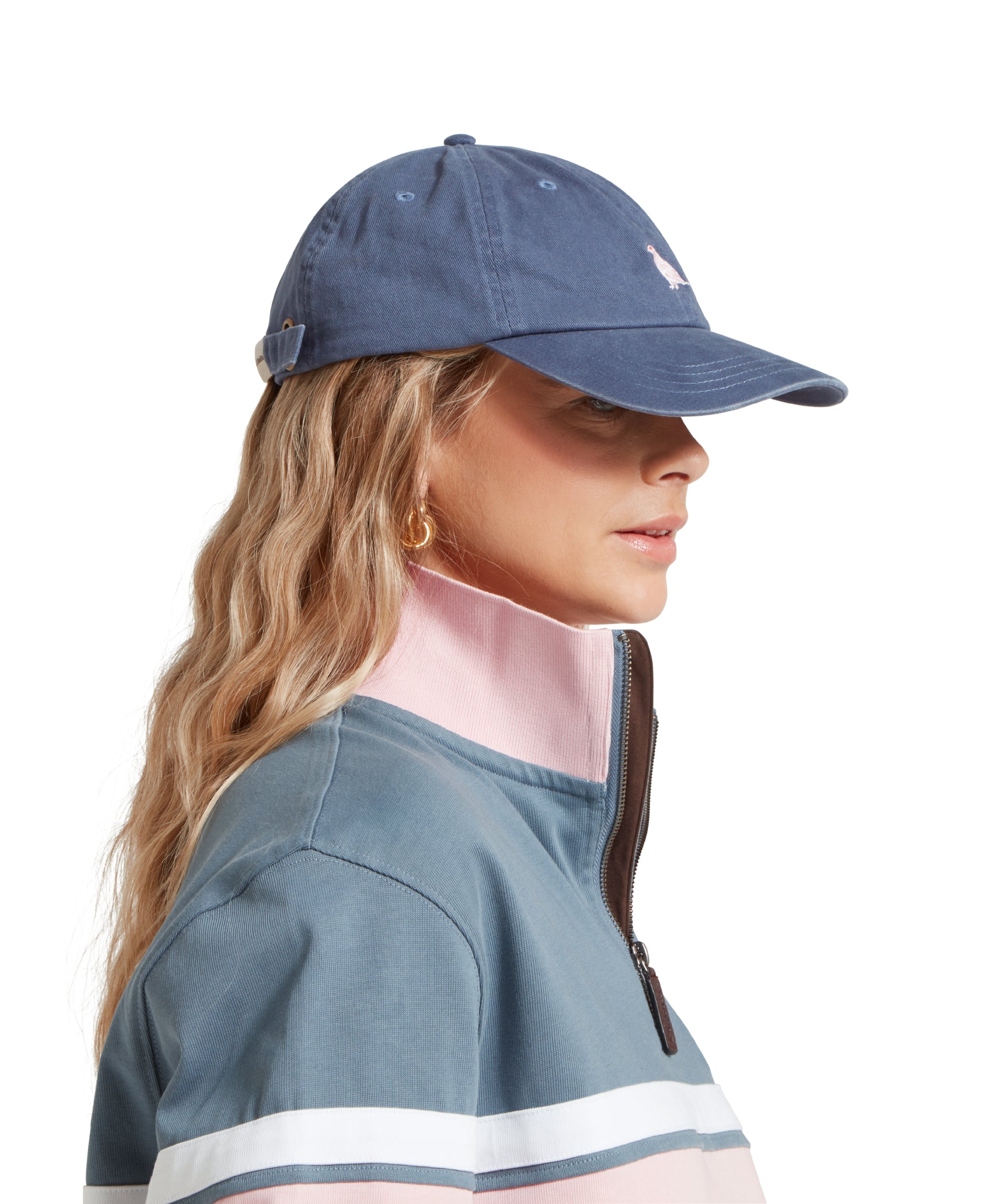 A side image of a female model wearing a mid blue cap with white embroidered bird logo on the front. It is paired with a light blue and pink sweatshirt and white shirt.