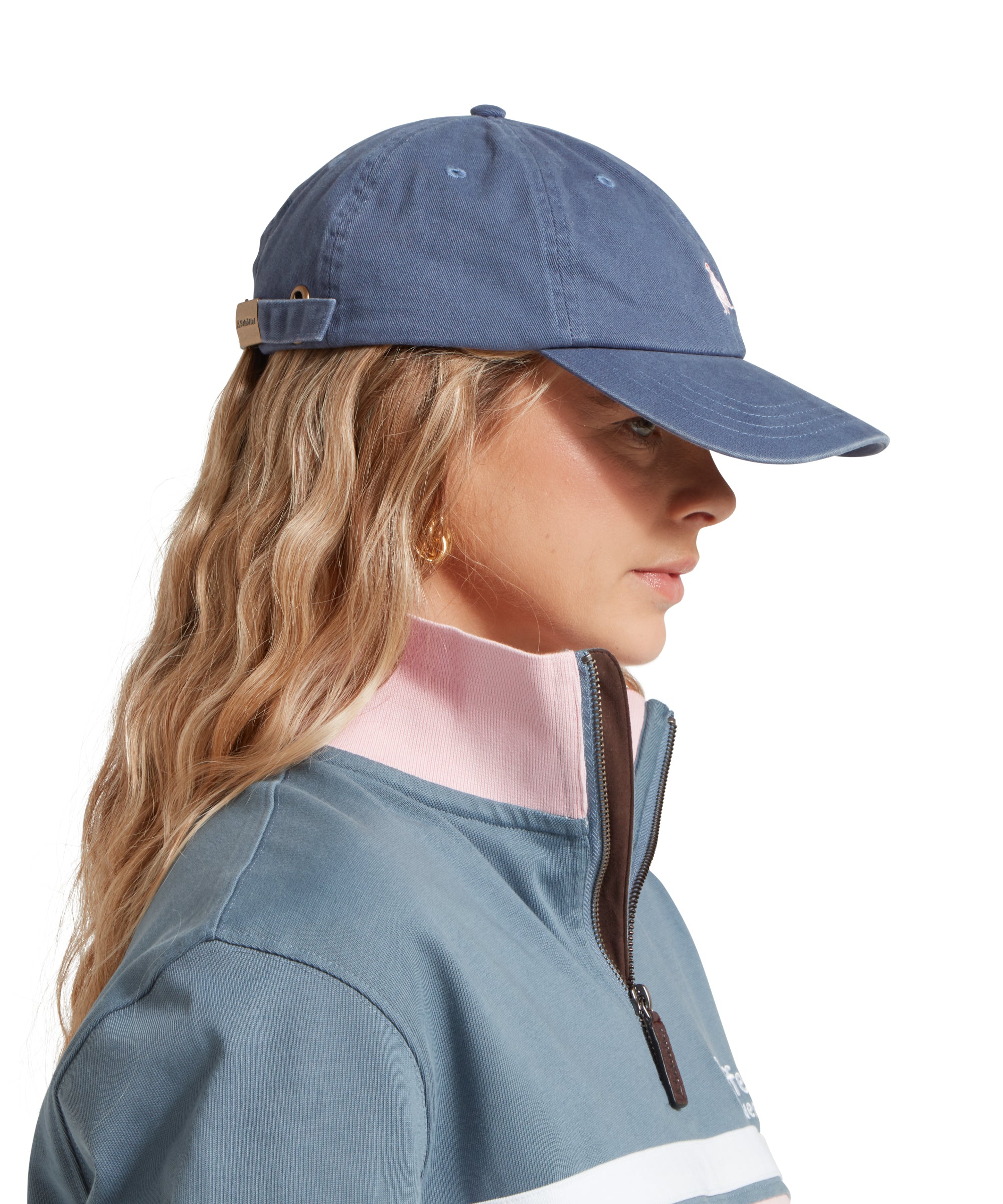 A side image of a female model wearing a mid blue cap with white embroidered bird logo on the front. It is paired with a light blue and pink sweatshirt and white shirt.